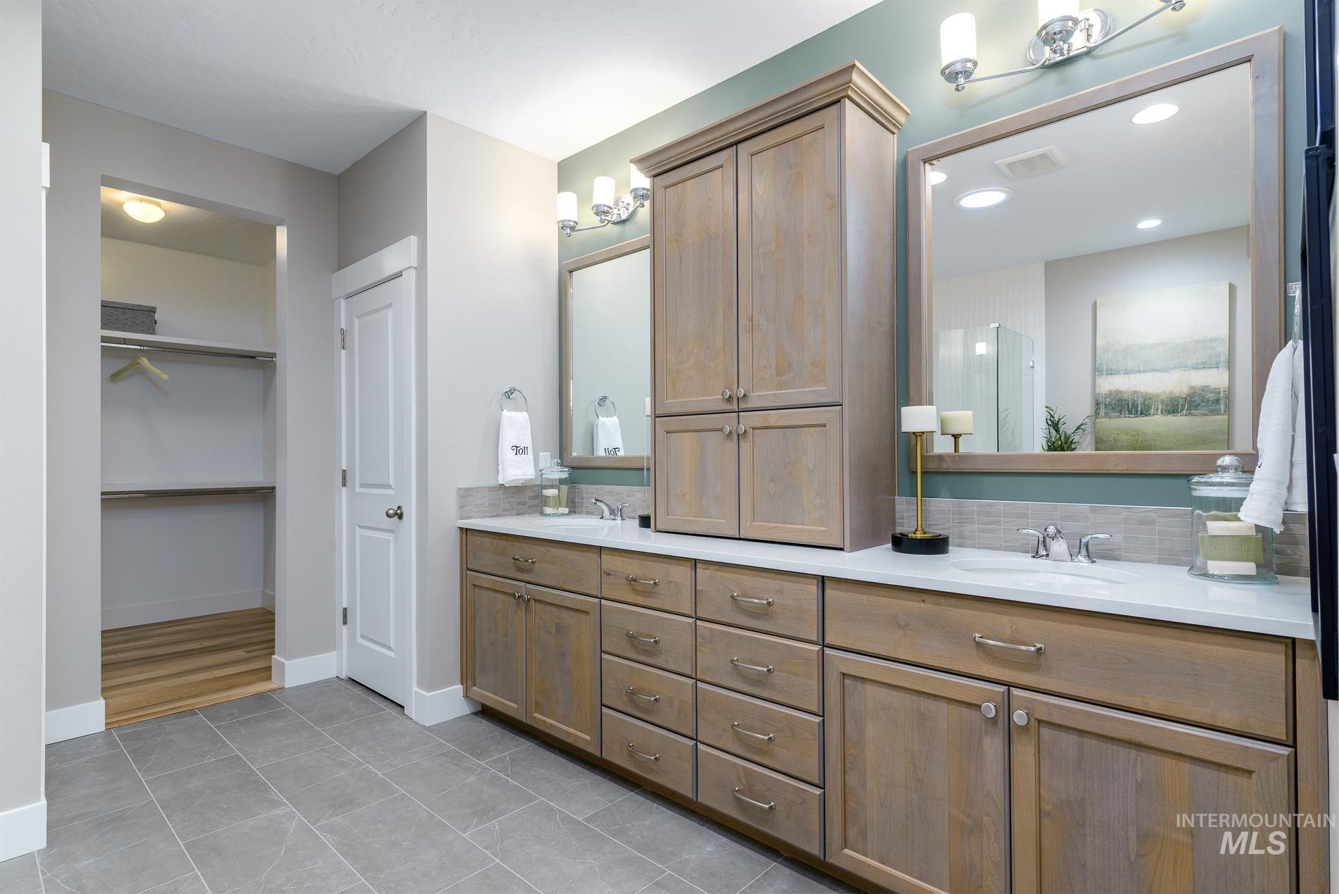 Full bath with double vanity, light tile patterned floors, and a walk in closet