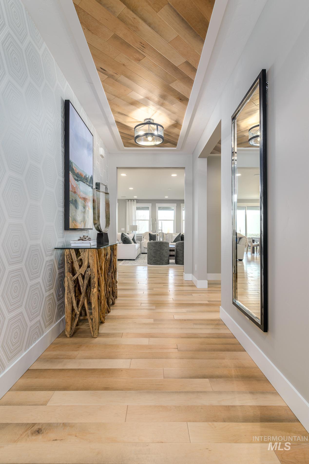 Corridor featuring wallpapered walls, light wood-style floors, wood ceiling, an accent wall, and a raised ceiling