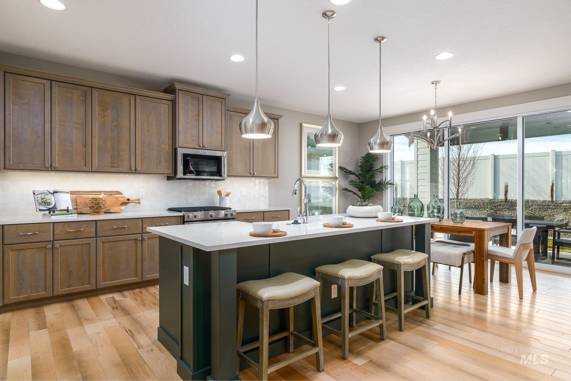 Kitchen with light wood-type flooring, hanging light fixtures, a center island with sink, recessed lighting, and a kitchen bar