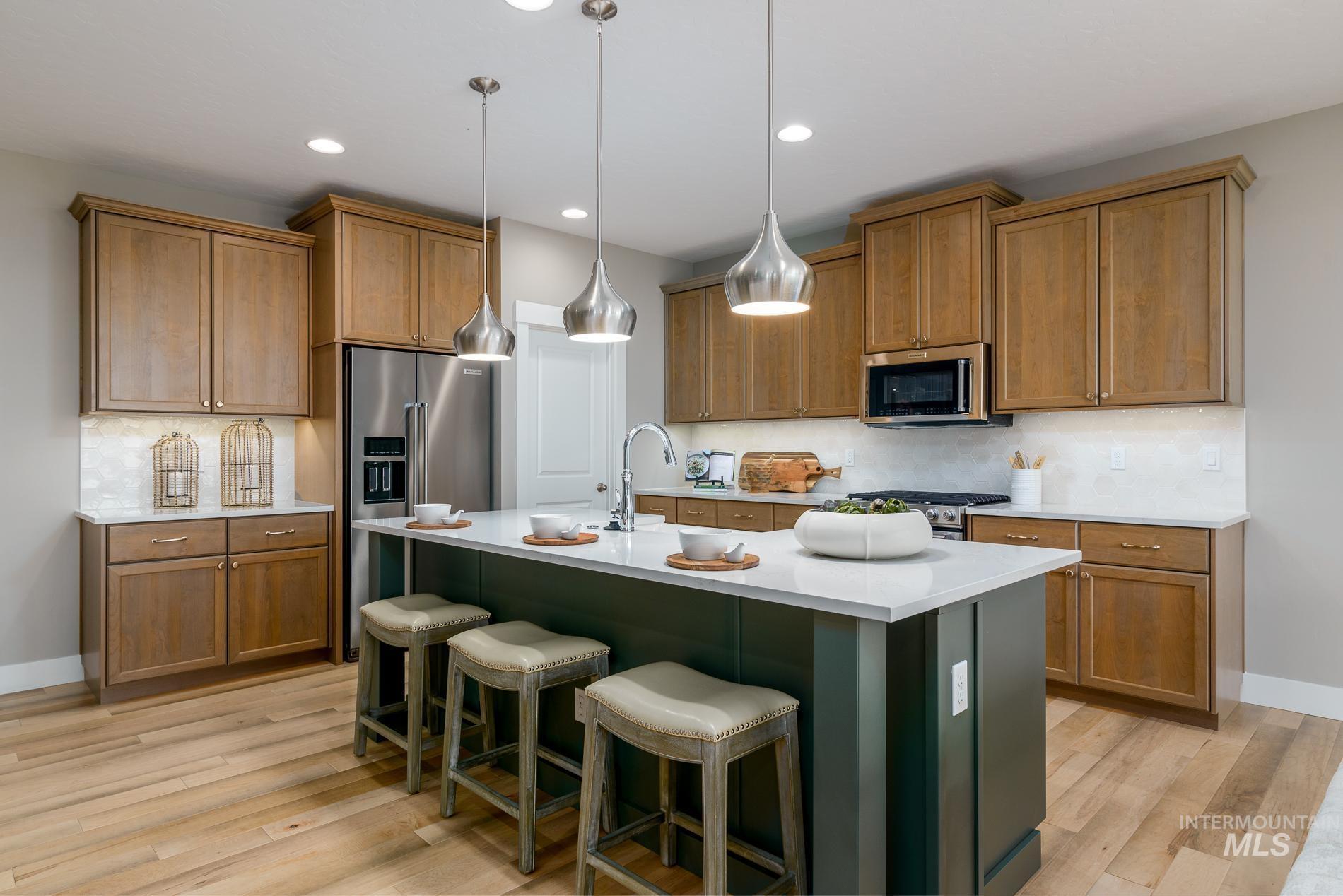 Kitchen with tasteful backsplash, brown cabinets, hanging light fixtures, an island with sink, and light wood-type flooring