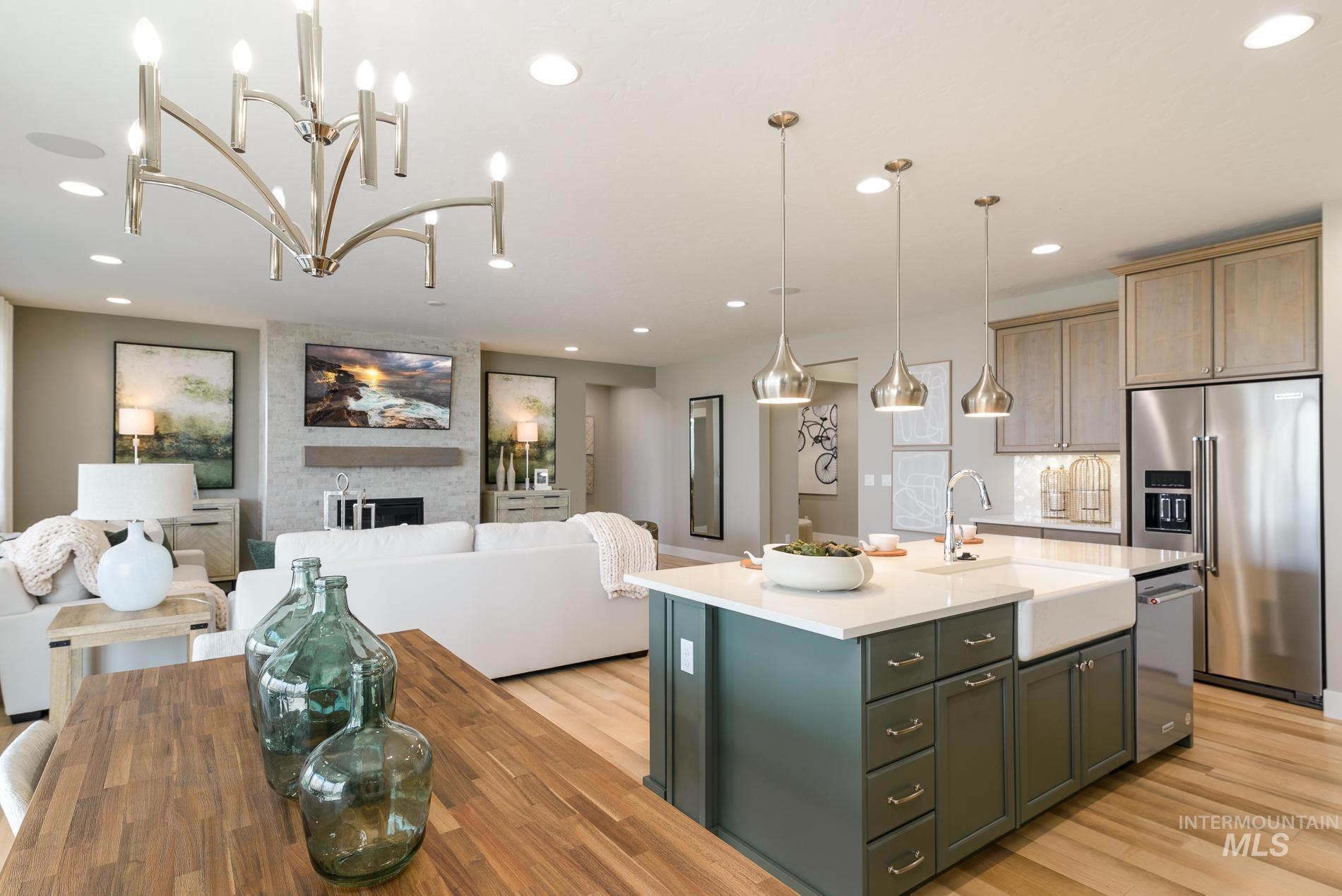 Kitchen with a large fireplace, a kitchen island with sink, open floor plan, appliances with stainless steel finishes, and decorative light fixtures
