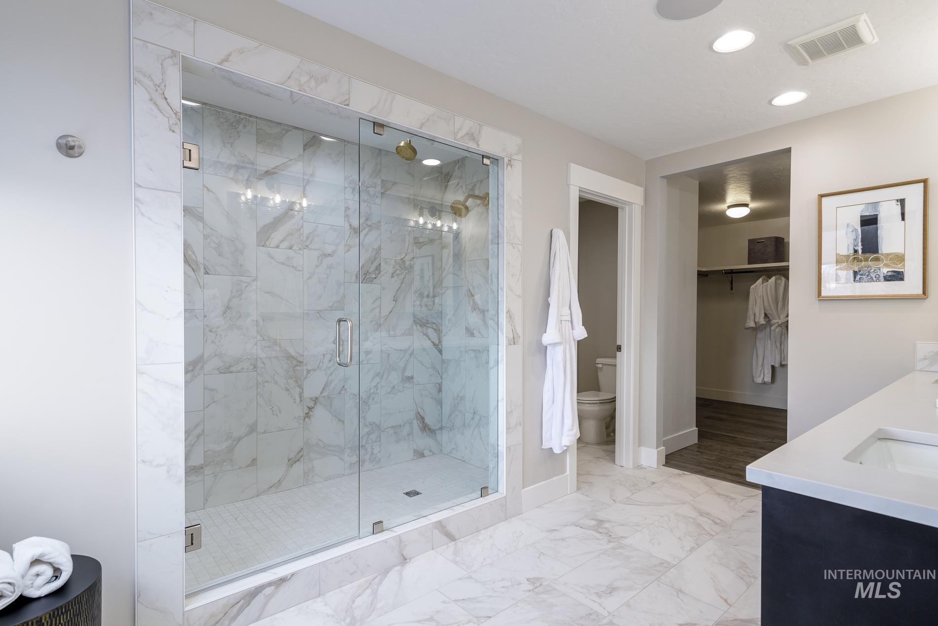 Full bath featuring light marble finish floors, a walk in closet, a marble finish shower, double vanity, and recessed lighting