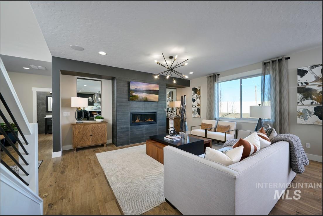 Living area with a tiled fireplace, a chandelier, wood finished floors, a textured ceiling, and recessed lighting
