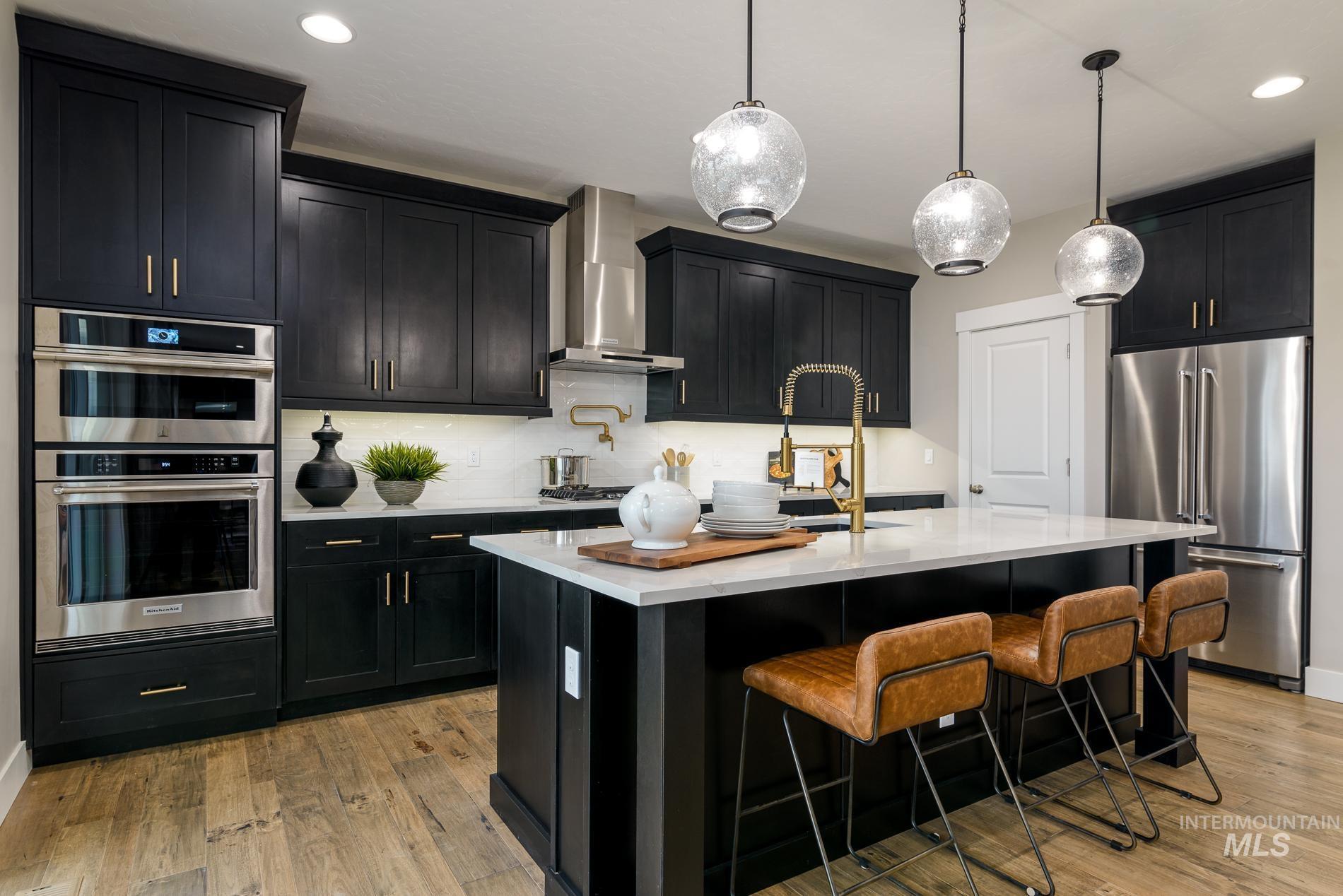 Kitchen featuring dark cabinetry, stainless steel appliances, light wood-style floors, light stone countertops, and recessed lighting