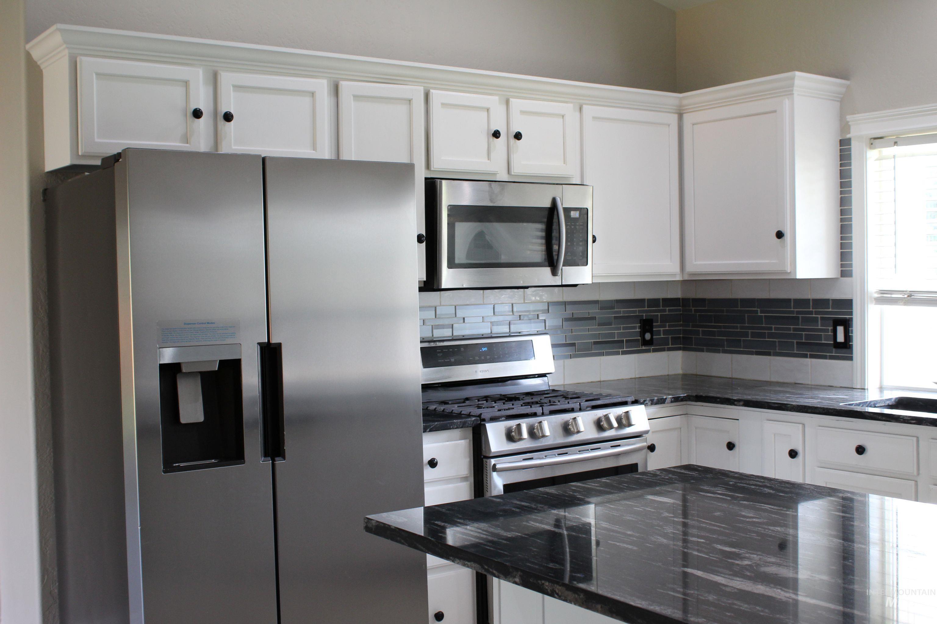 Kitchen featuring stainless steel appliances, dark stone counters, white cabinetry, and backsplash