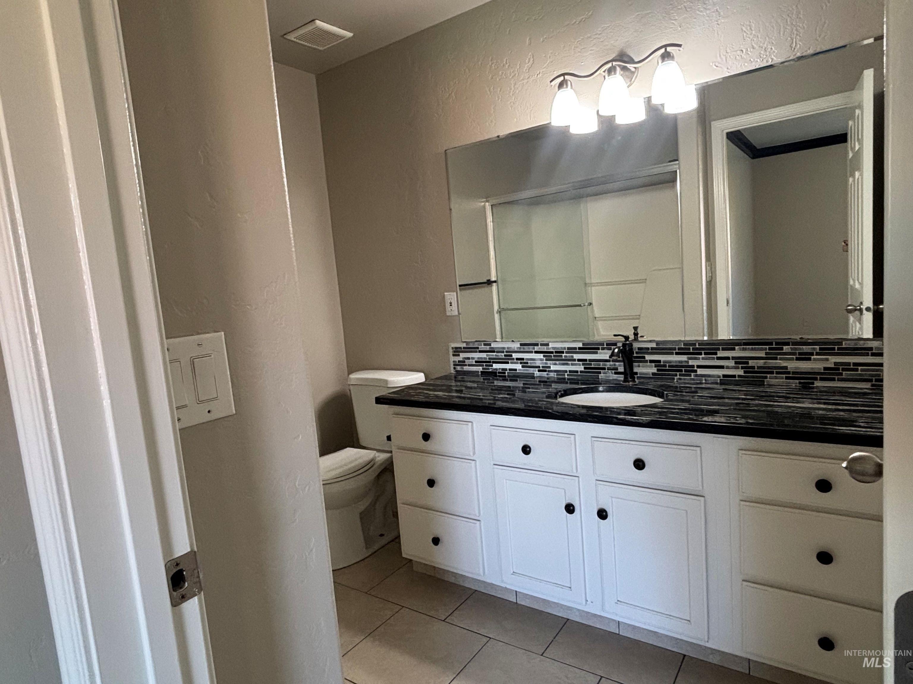 Bathroom featuring a textured wall, light tile patterned flooring, vanity, and tasteful backsplash