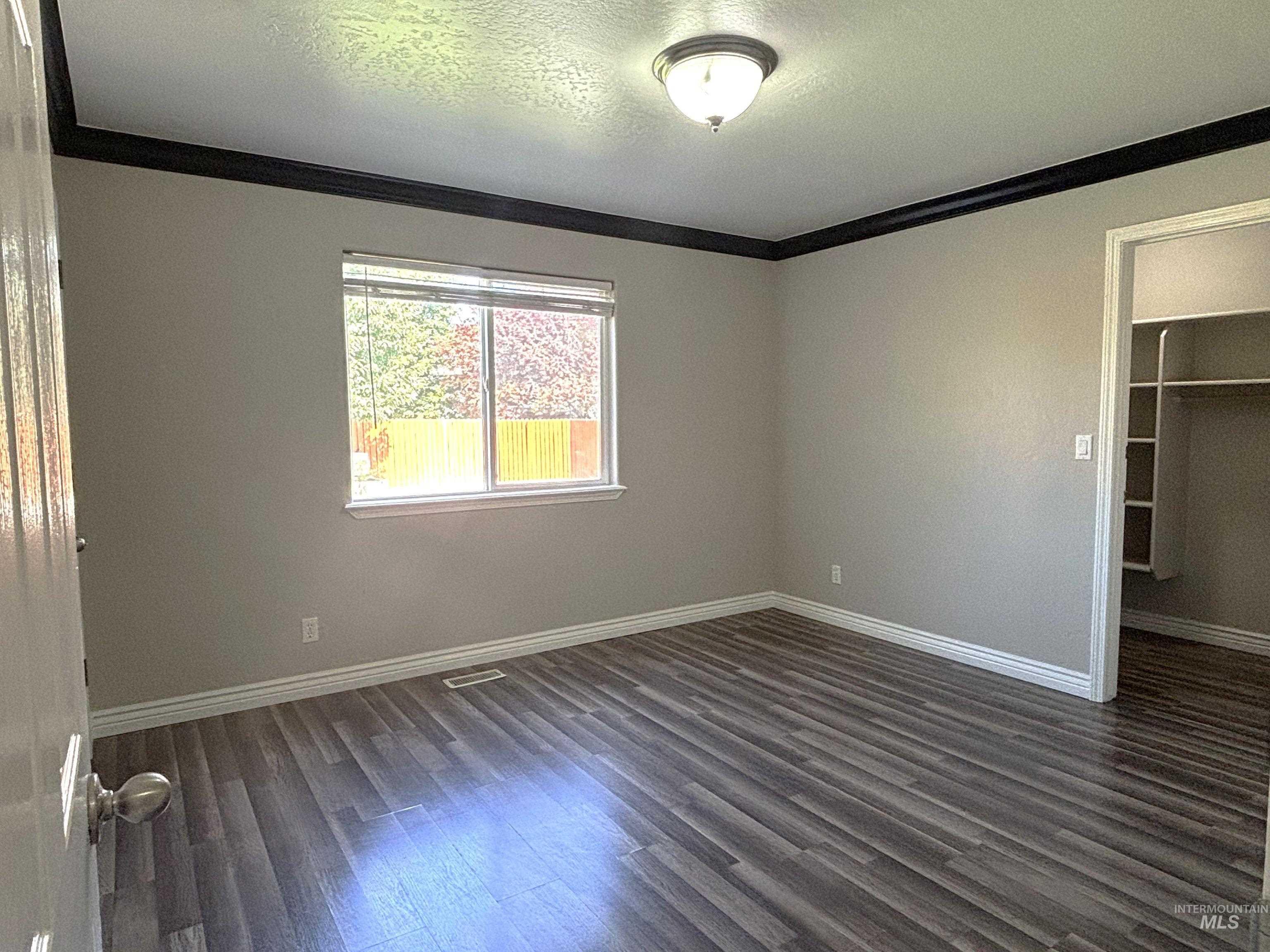 Unfurnished bedroom featuring a textured ceiling, a walk in closet, crown molding, and dark wood-style floors