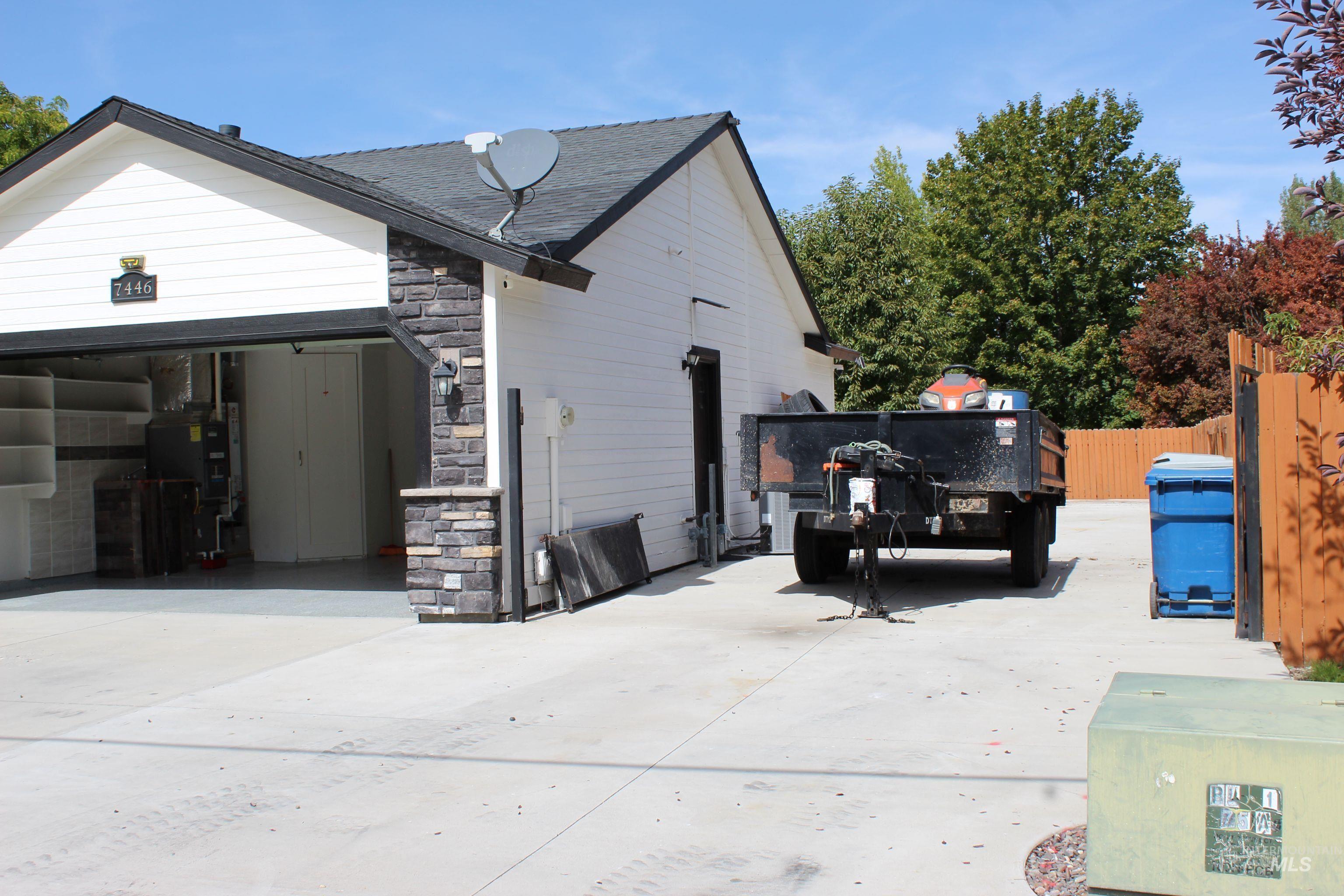 View of home's exterior with stone siding, concrete driveway, roof with shingles, and heating unit