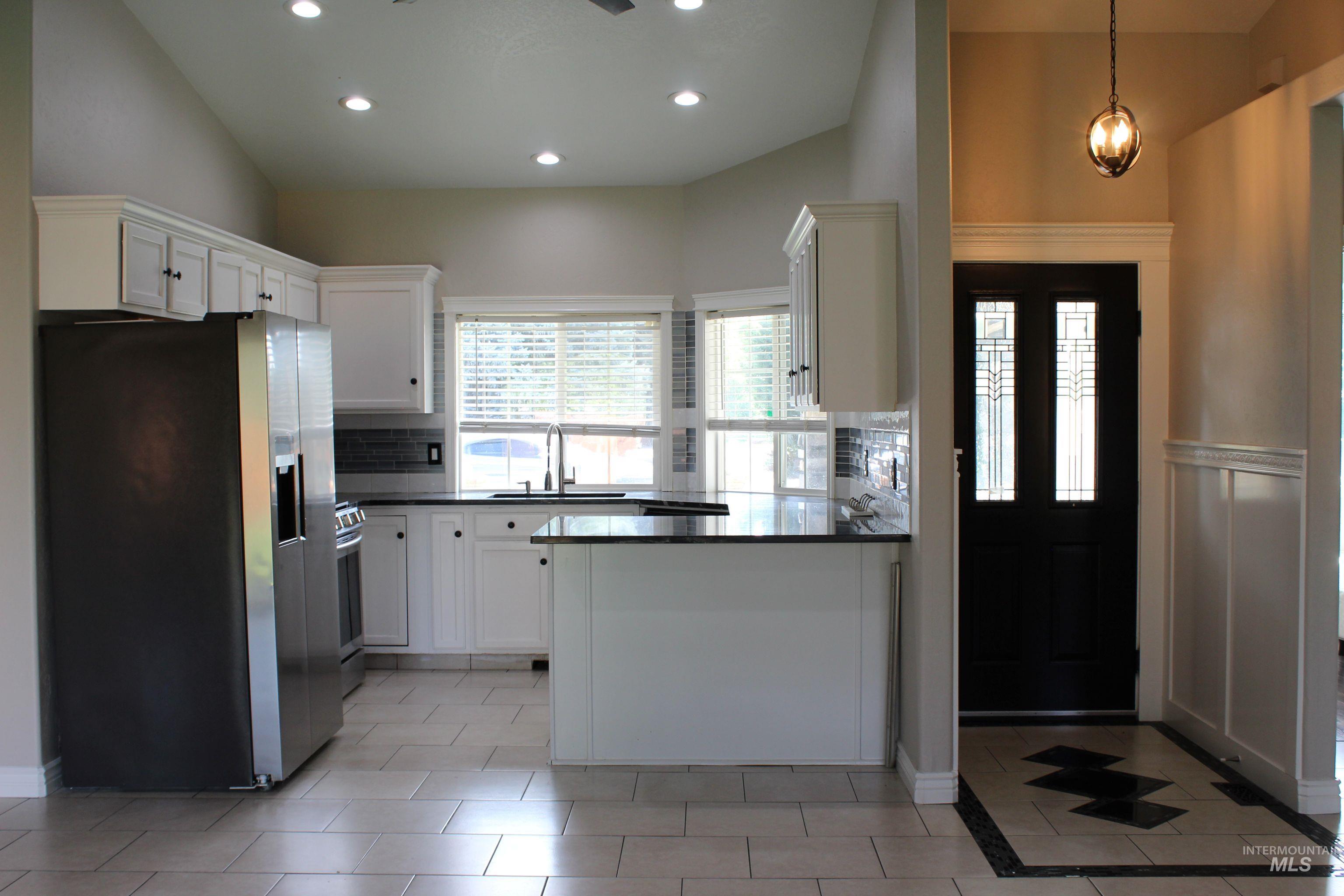 Kitchen featuring appliances with stainless steel finishes, white cabinets, a peninsula, tasteful backsplash, and light tile patterned flooring