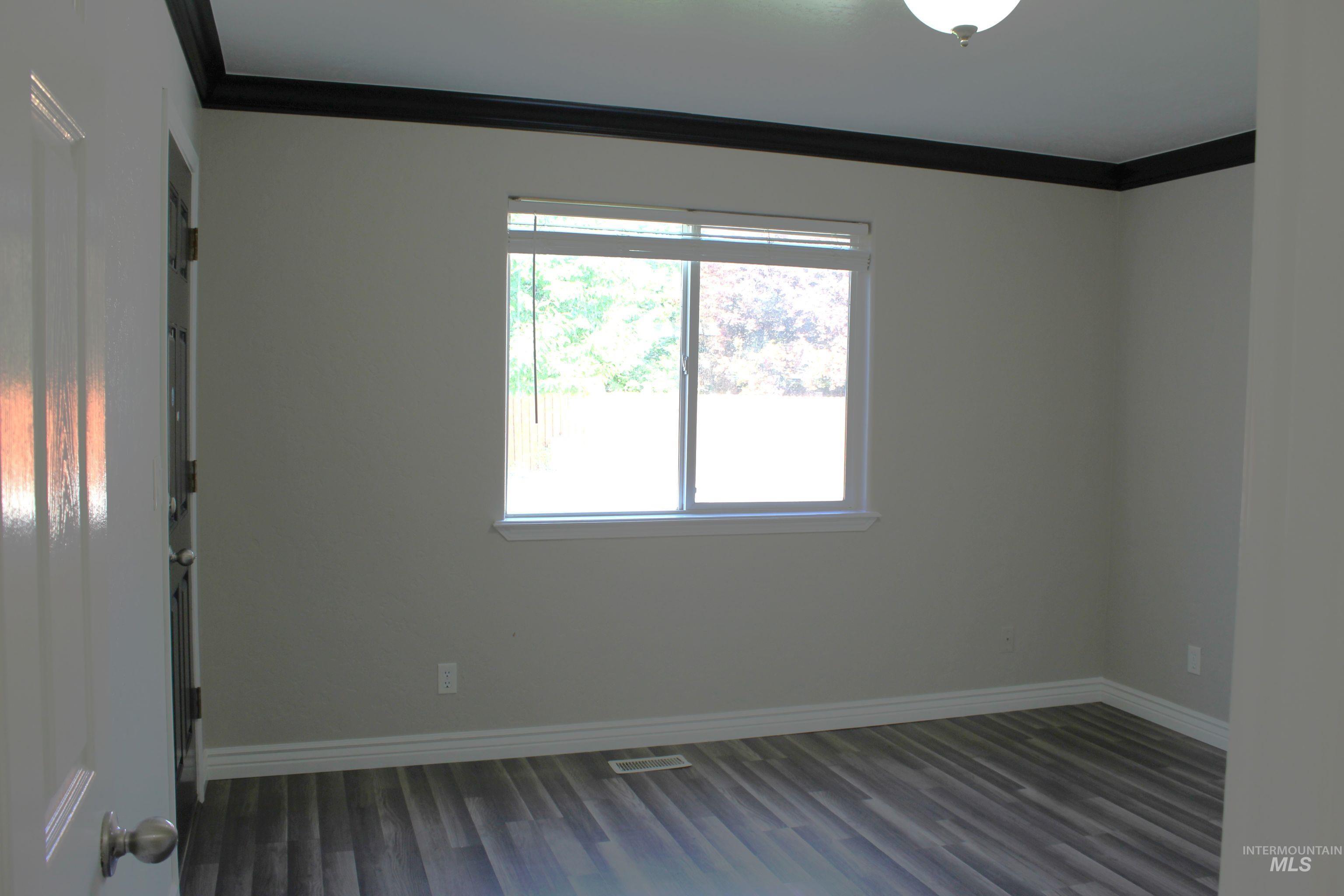 Empty room featuring crown molding and dark wood-style flooring