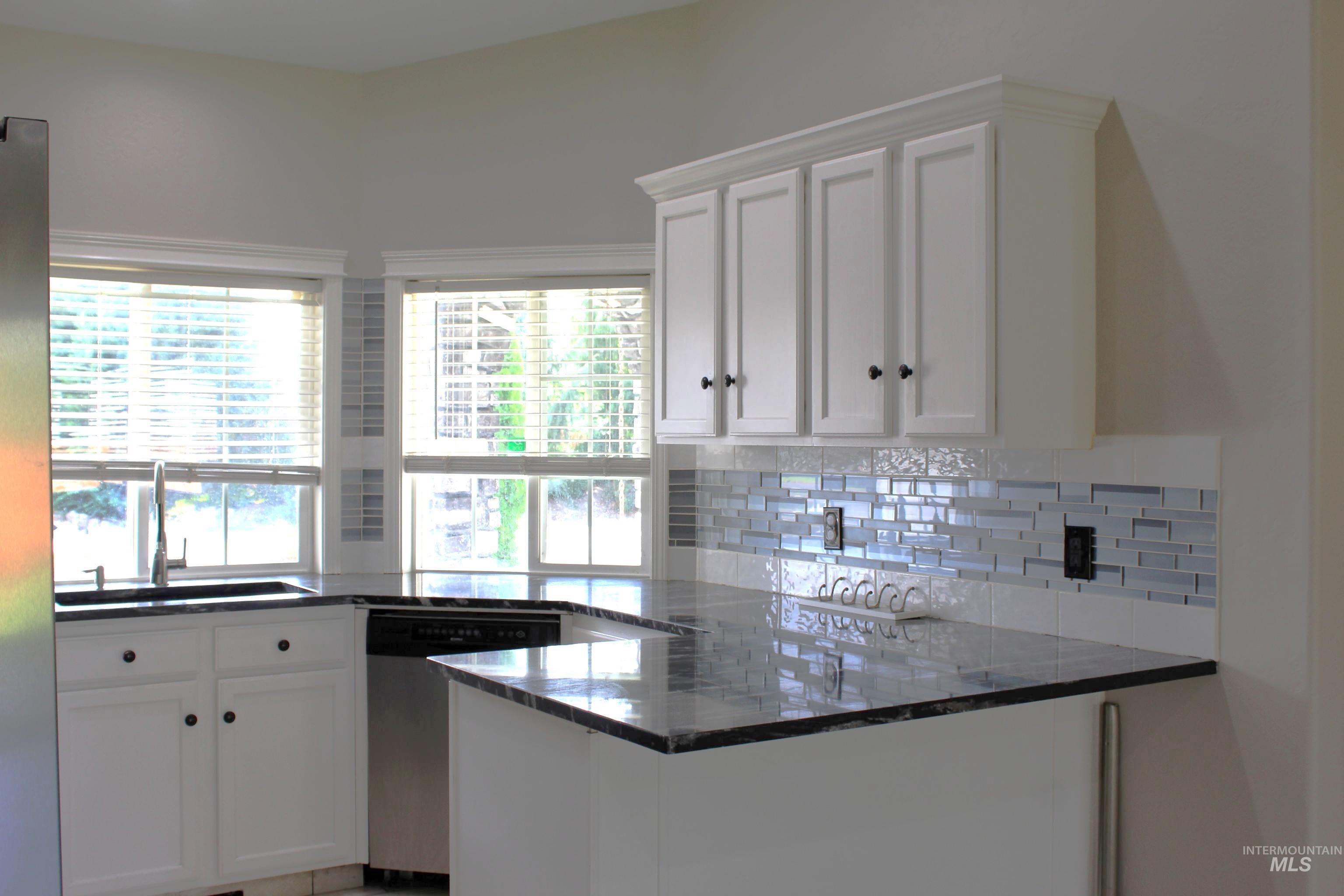 Kitchen featuring white cabinetry, a peninsula, appliances with stainless steel finishes, and dark stone countertops