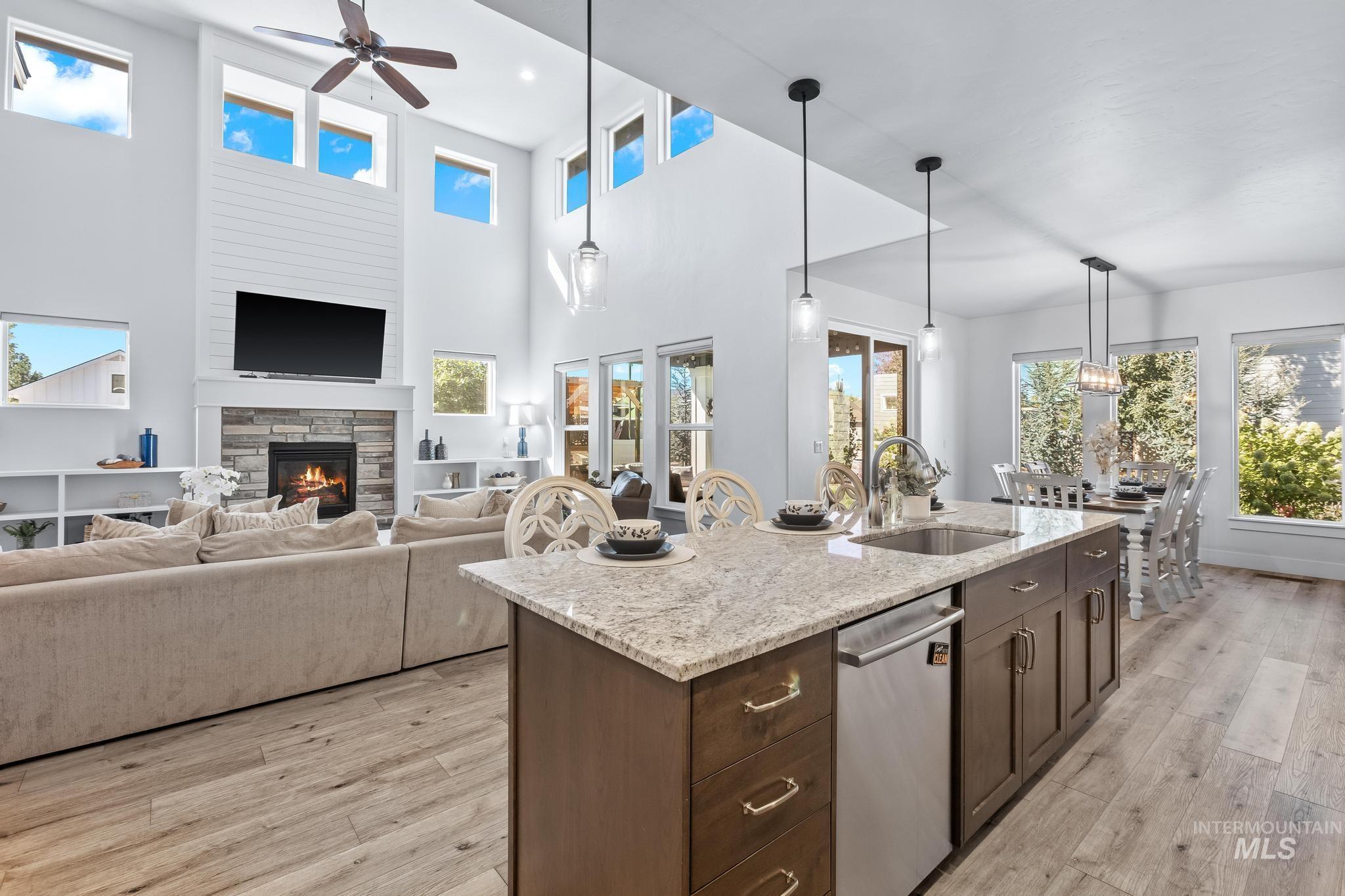 Kitchen featuring dark brown cabinets, light stone counters, pendant lighting, a stone fireplace, and dishwasher