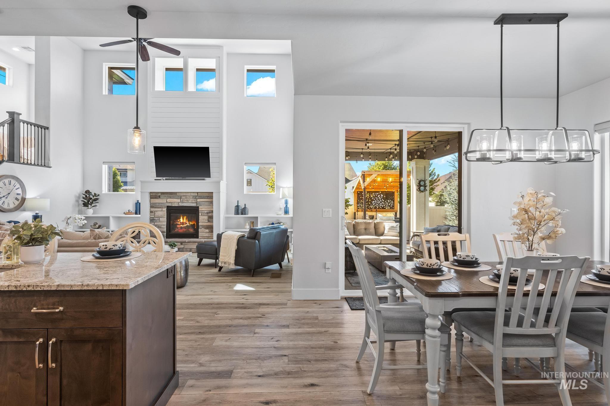 Dining space with a stone fireplace, light wood finished floors, a ceiling fan, and a towering ceiling