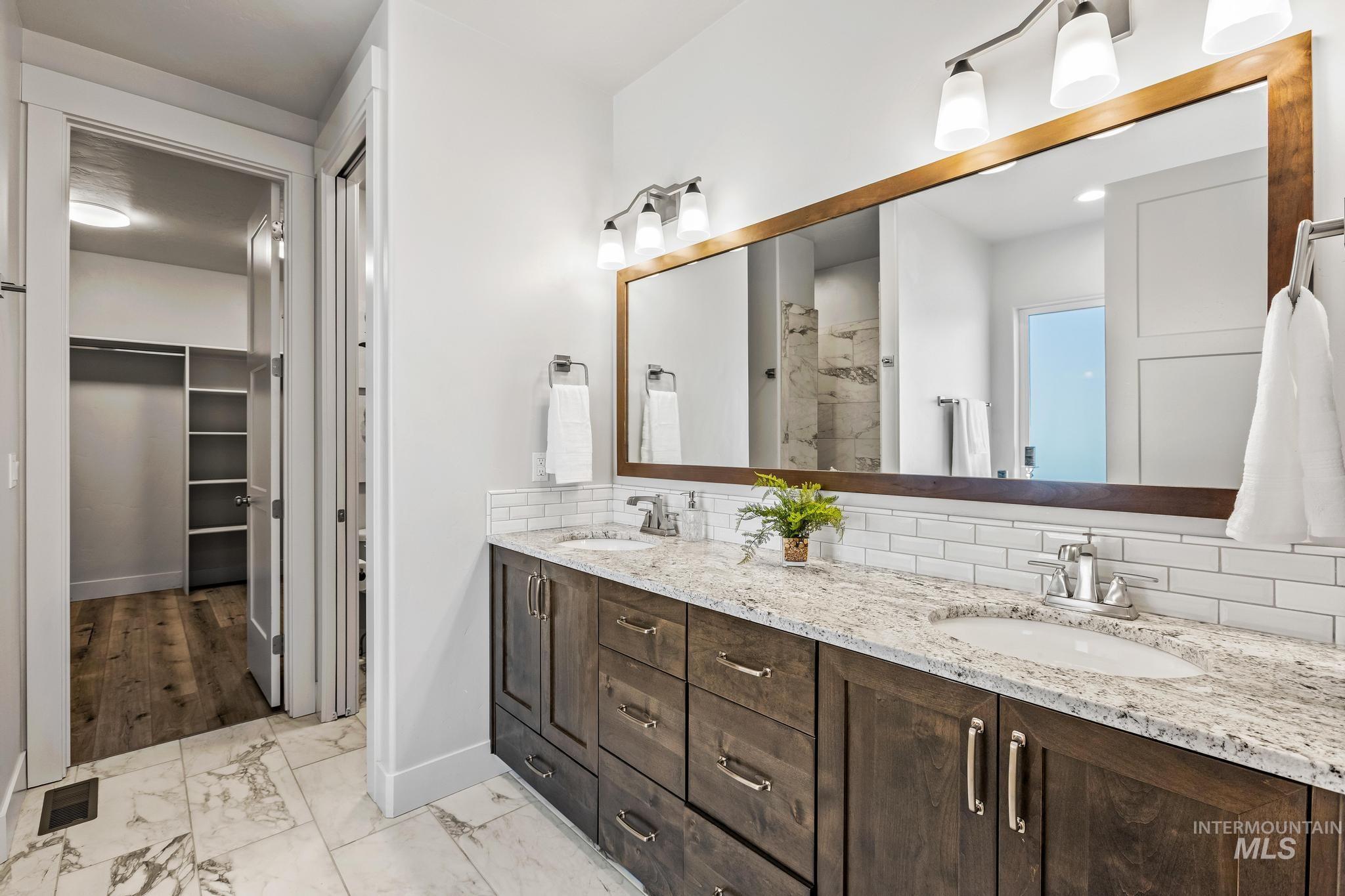 Full bath featuring a walk in closet, light marble finish flooring, double vanity, tiled shower, and tasteful backsplash