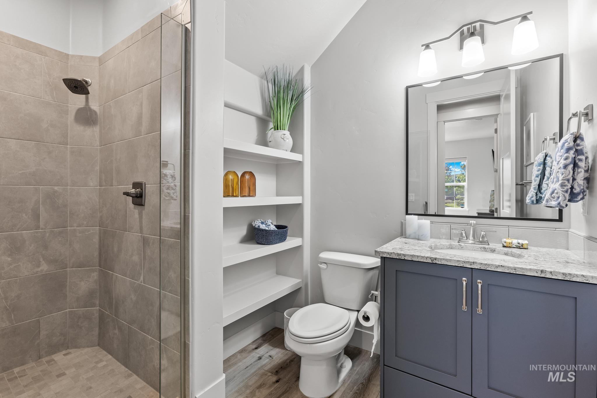 Full bath with a stall shower, vanity, light wood-style floors, and built in shelves