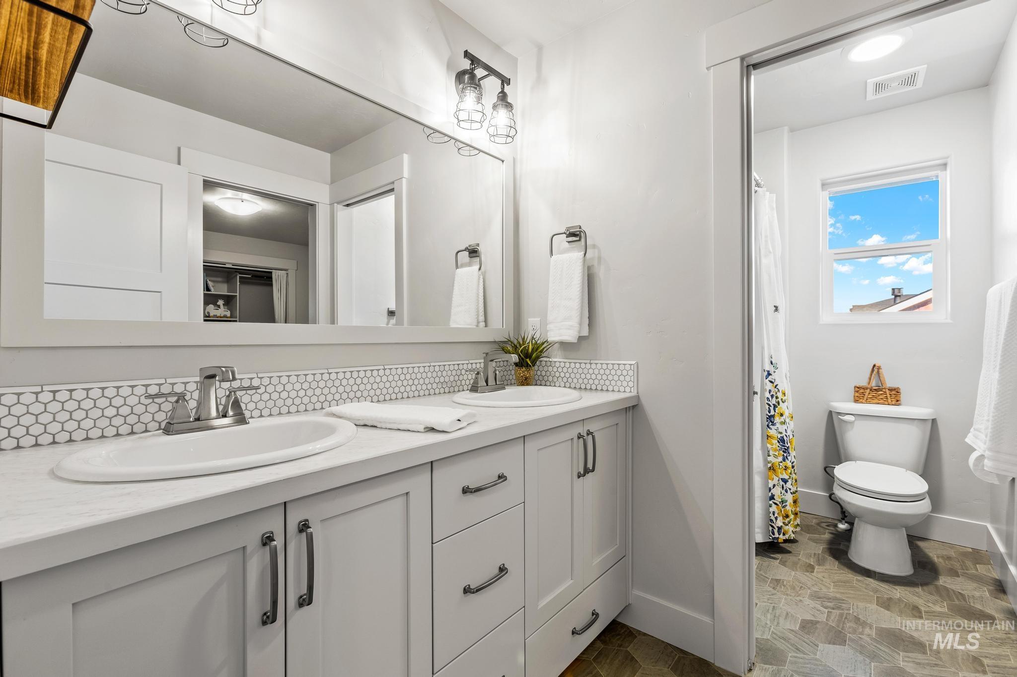 Bathroom with double vanity, dark stone finish floors, and backsplash
