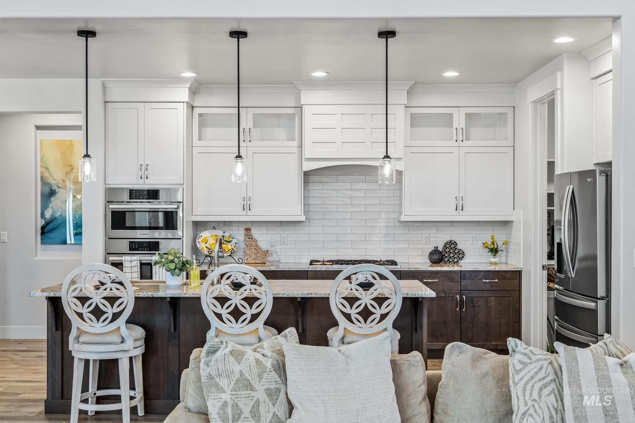 Kitchen with glass insert cabinets, light stone counters, backsplash, white cabinets, and a kitchen bar