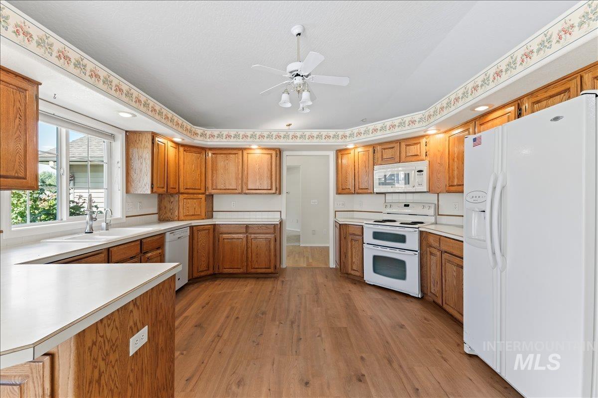 Kitchen with white appliances, light wood finished floors, light countertops, and brown cabinetry