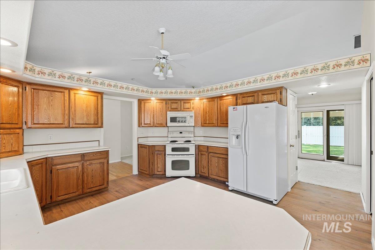 Kitchen with white appliances, light wood-type flooring, light countertops, and brown cabinets