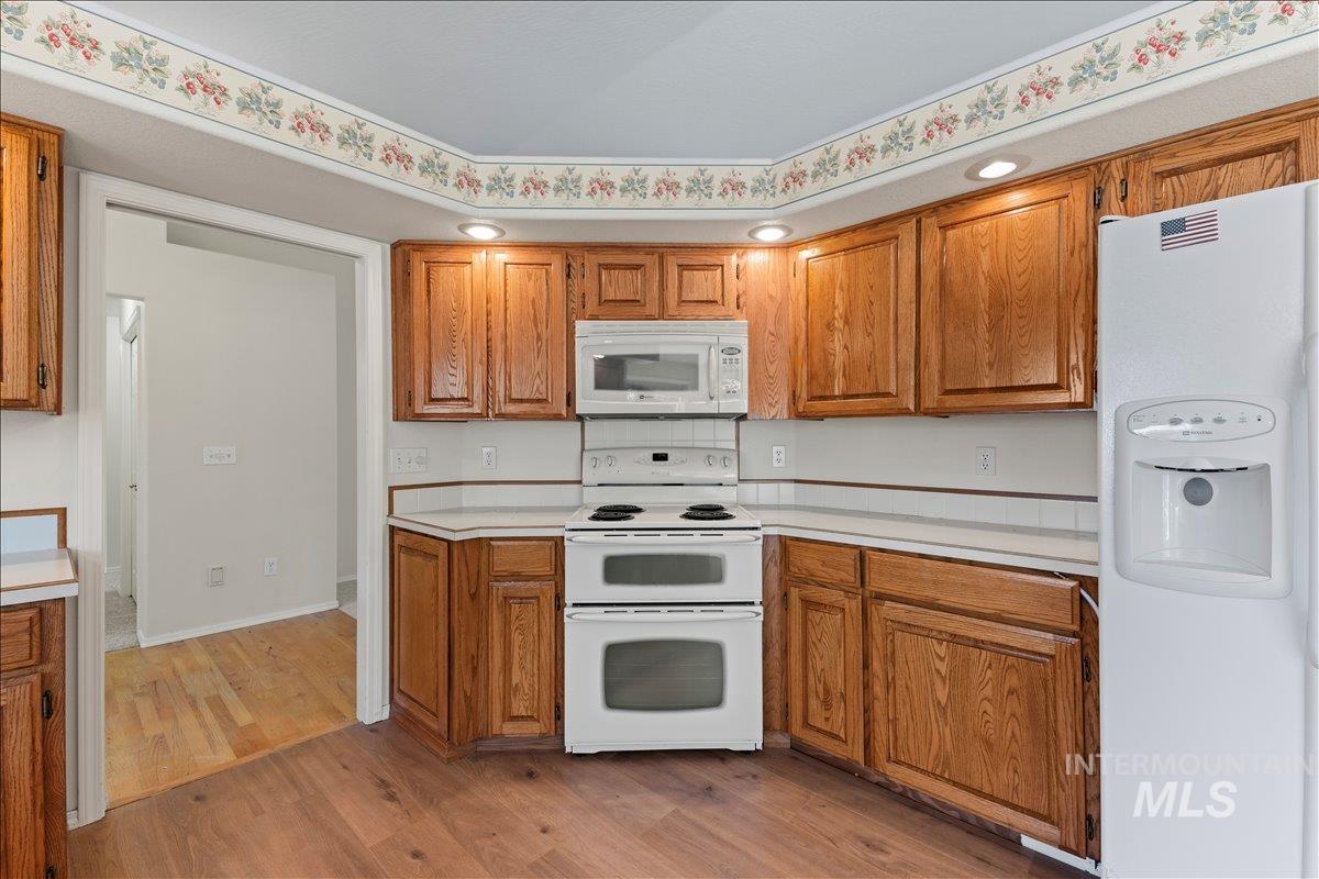 Kitchen with white appliances, light wood-style flooring, light countertops, and brown cabinetry