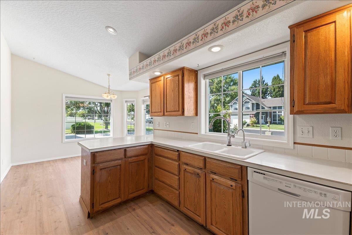 Kitchen with brown cabinets, dishwasher, light countertops, light wood-type flooring, and pendant lighting