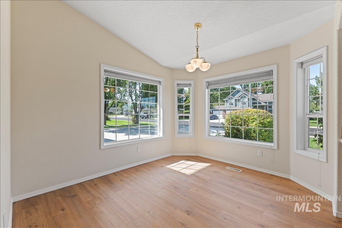 Unfurnished dining area with light wood finished floors, healthy amount of natural light, a textured ceiling, a chandelier, and lofted ceiling