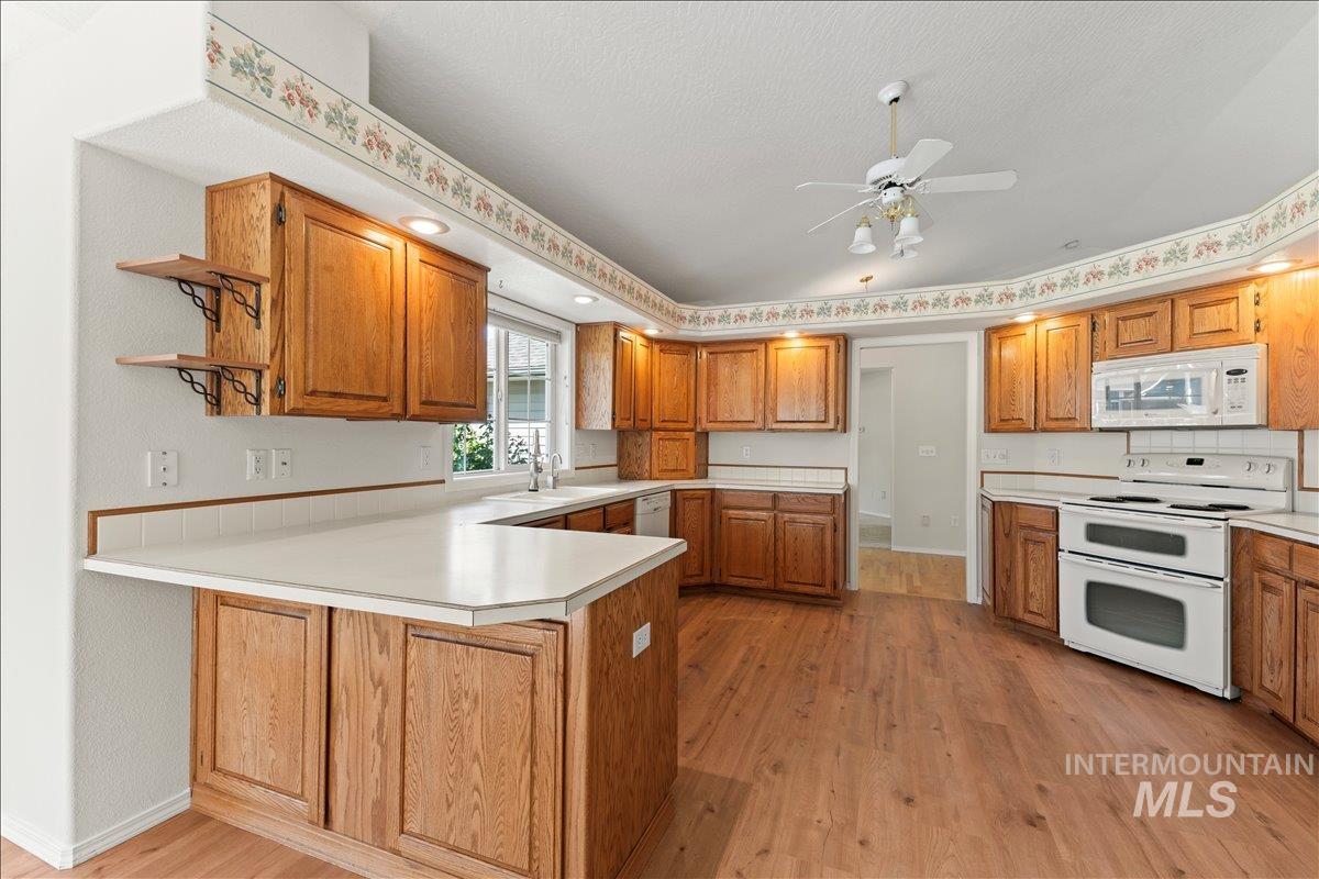 Kitchen featuring light wood-style flooring, light countertops, a peninsula, white appliances, and brown cabinetry