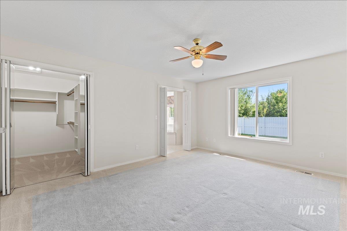 Unfurnished bedroom featuring a walk in closet, light colored carpet, and a ceiling fan