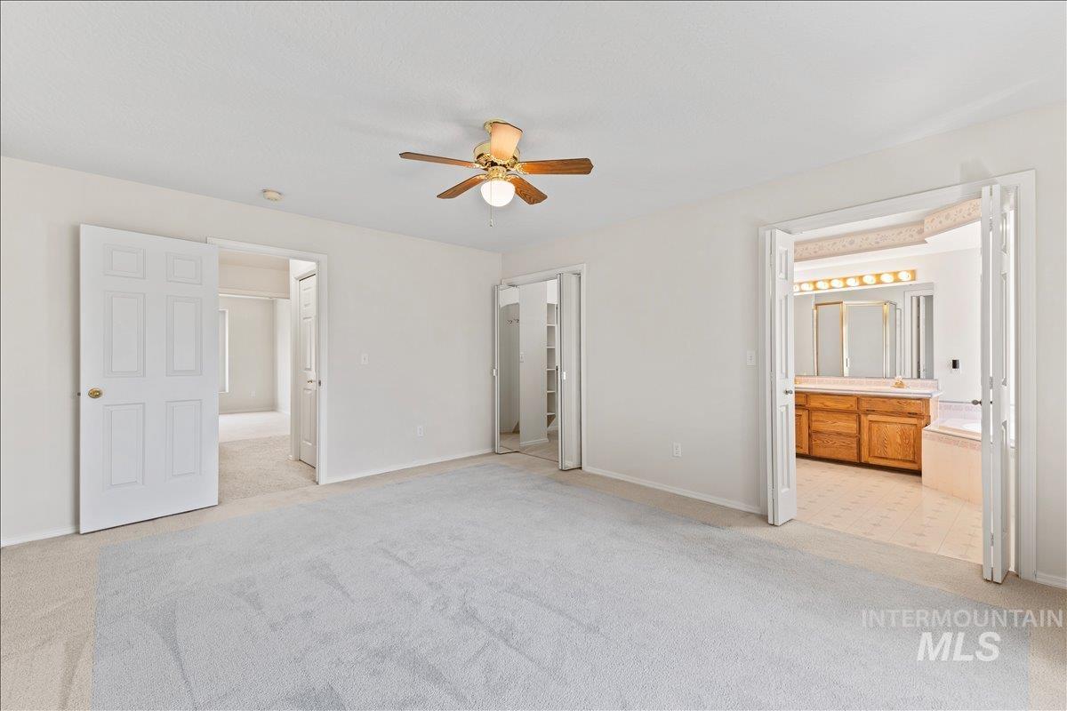 Unfurnished bedroom with light colored carpet, ensuite bath, and ceiling fan