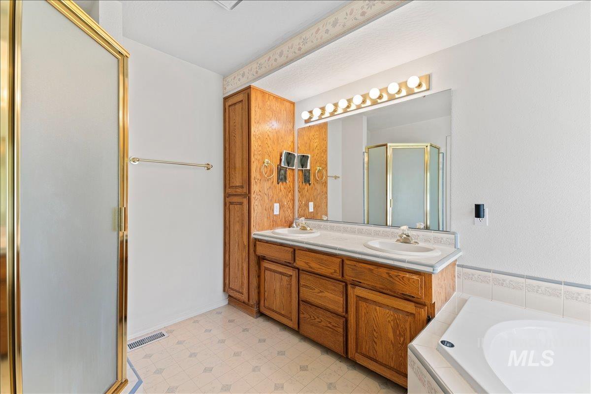 Full bathroom with double vanity, a stall shower, a bath, and light floors