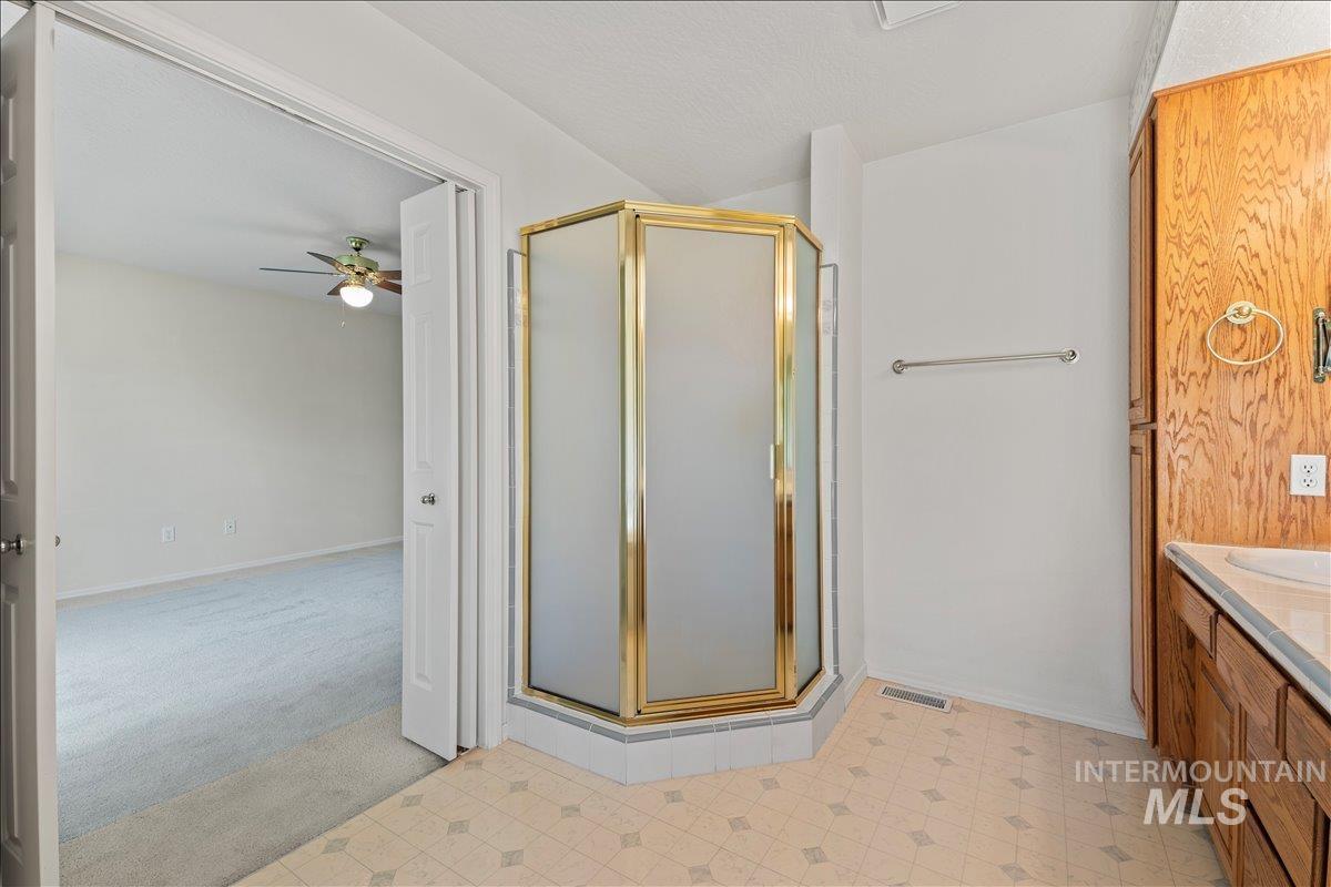 Full bath featuring vanity, a shower stall, ceiling fan, light floors, and a textured ceiling
