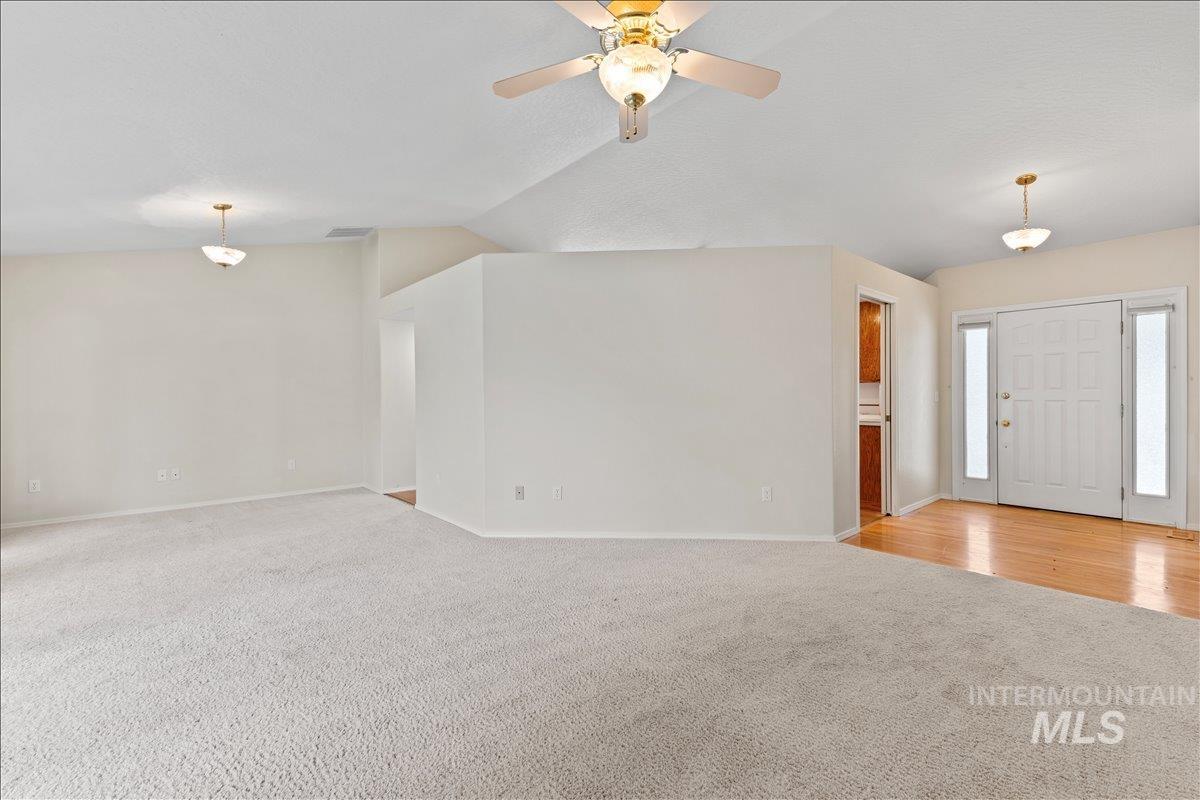 Unfurnished living room with light colored carpet, vaulted ceiling, and ceiling fan