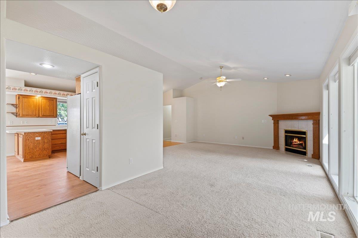 Unfurnished living room with light colored carpet, a tile fireplace, lofted ceiling, recessed lighting, and ceiling fan