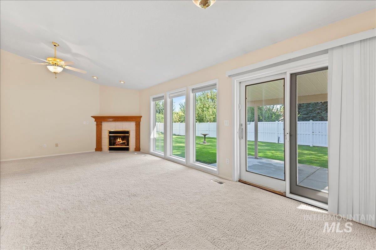 Unfurnished living room with carpet floors, vaulted ceiling, a fireplace, and ceiling fan