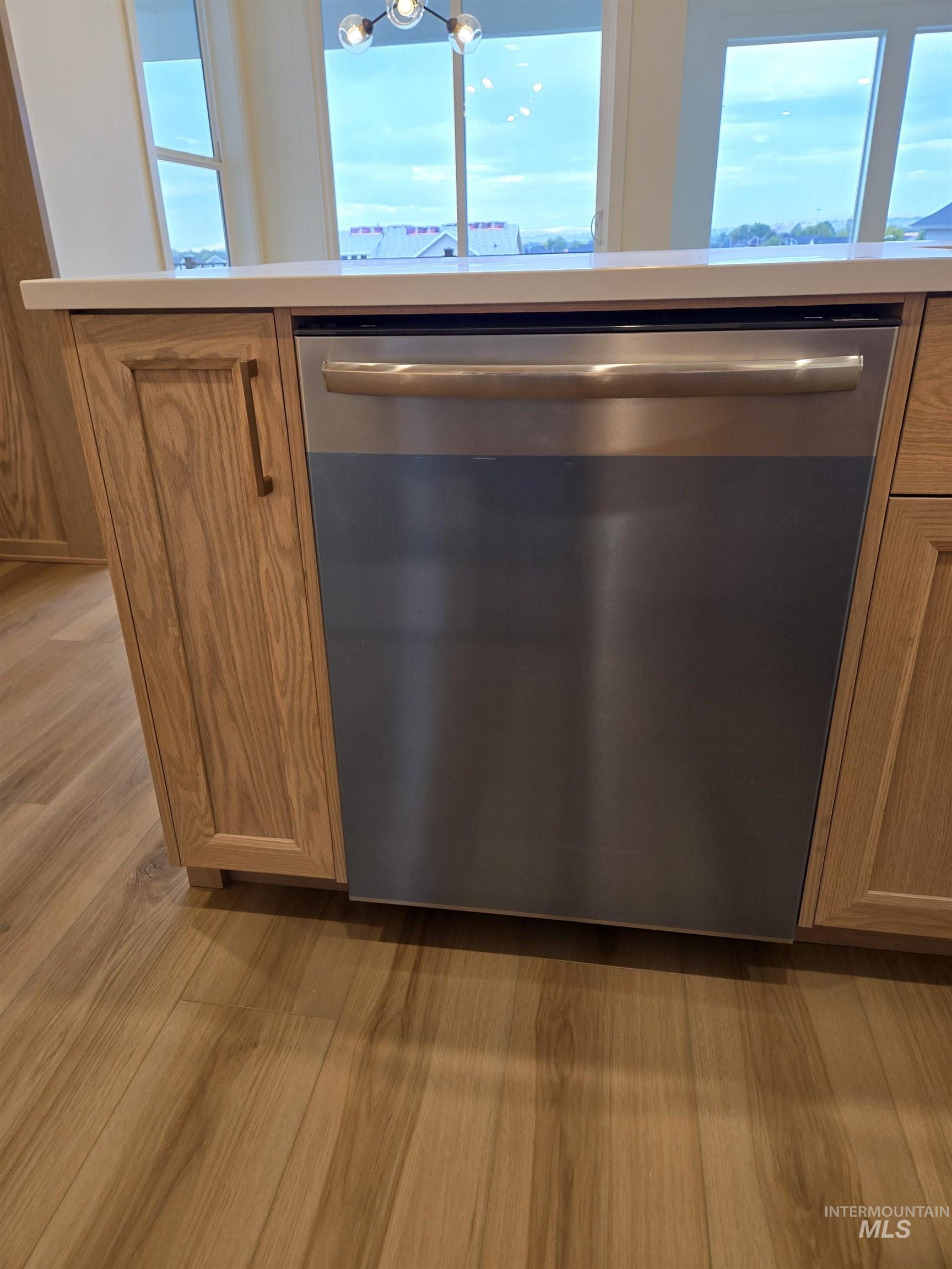 Kitchen view of stainless steel dishwasher, brown cabinetry, light countertops, and light wood-style floors