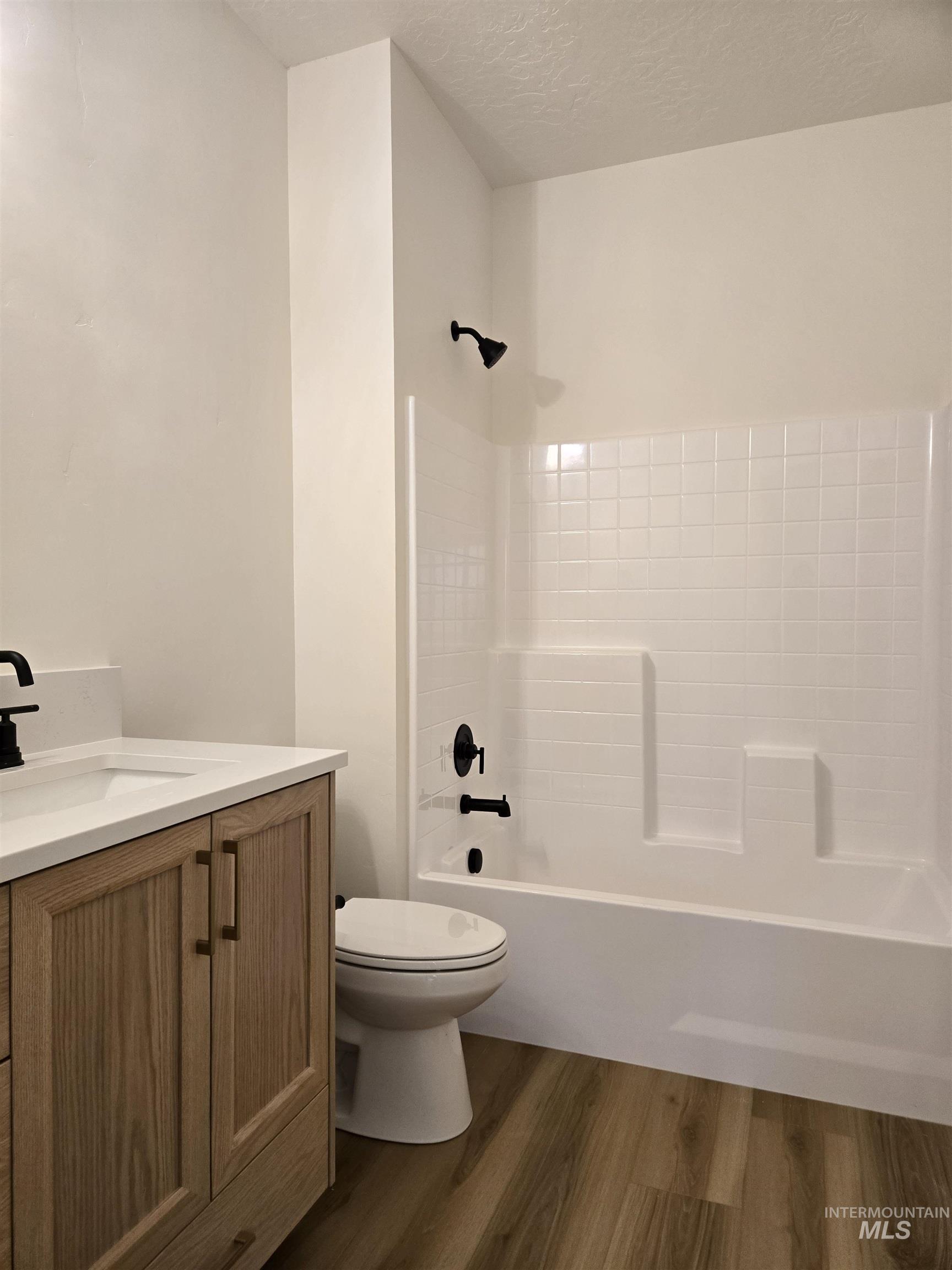 Bathroom with vanity, shower / bath combination, dark wood finished floors, and a textured ceiling