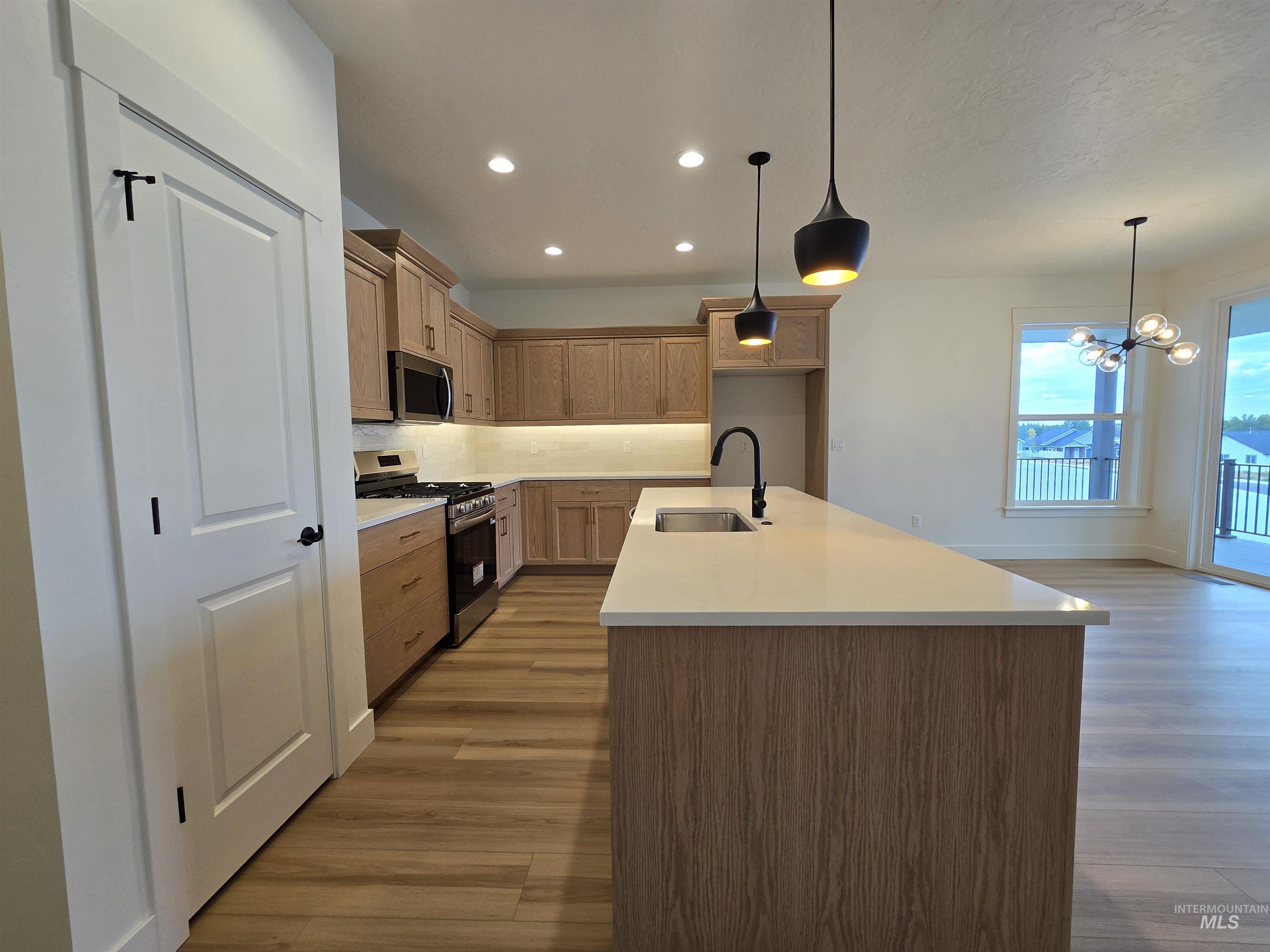 Kitchen with recessed lighting, appliances with stainless steel finishes, pendant lighting, an island with sink, and a chandelier