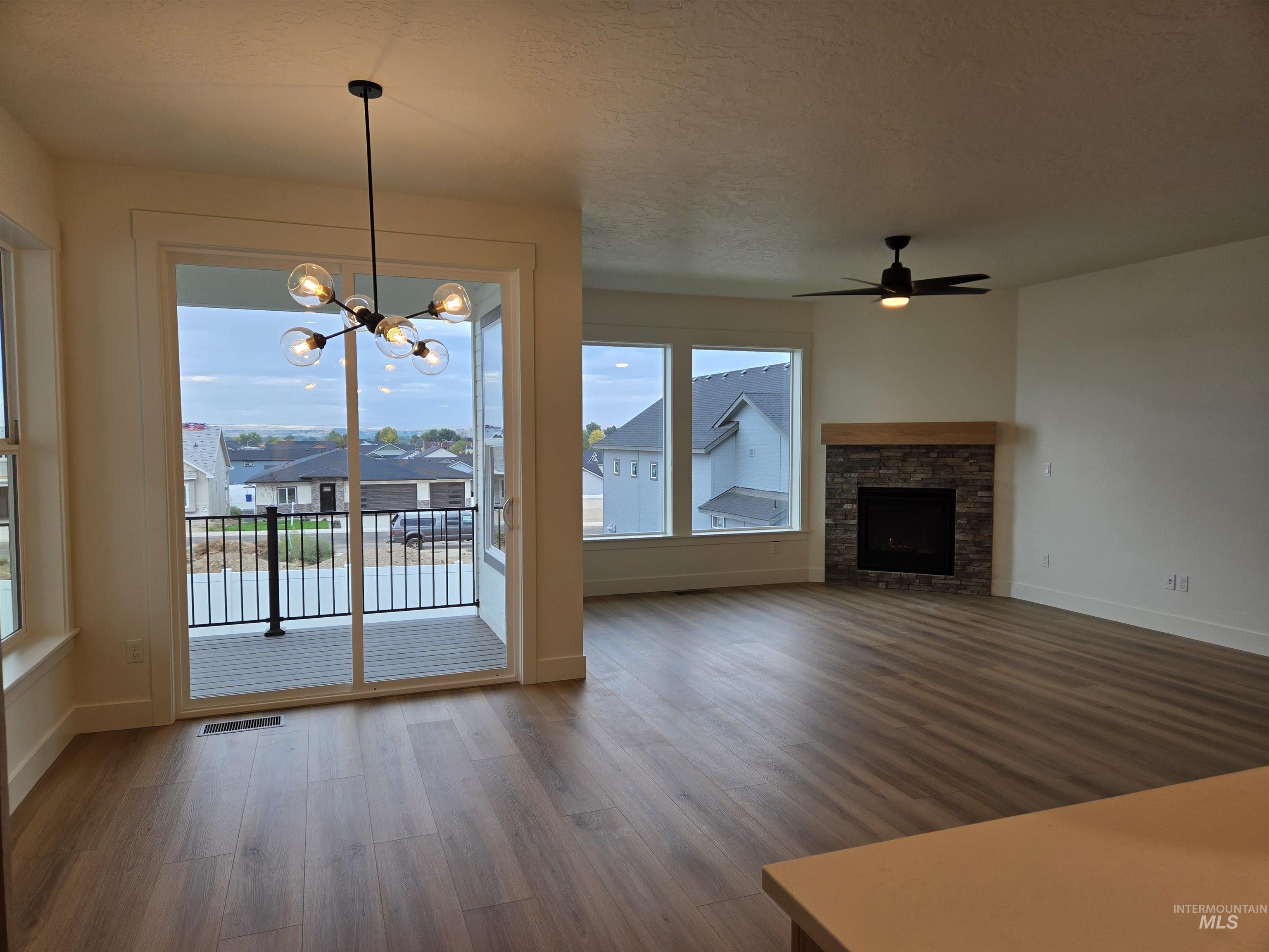 Unfurnished living room featuring dark wood-type flooring, a chandelier, ceiling fan, a stone fireplace, and a textured ceiling