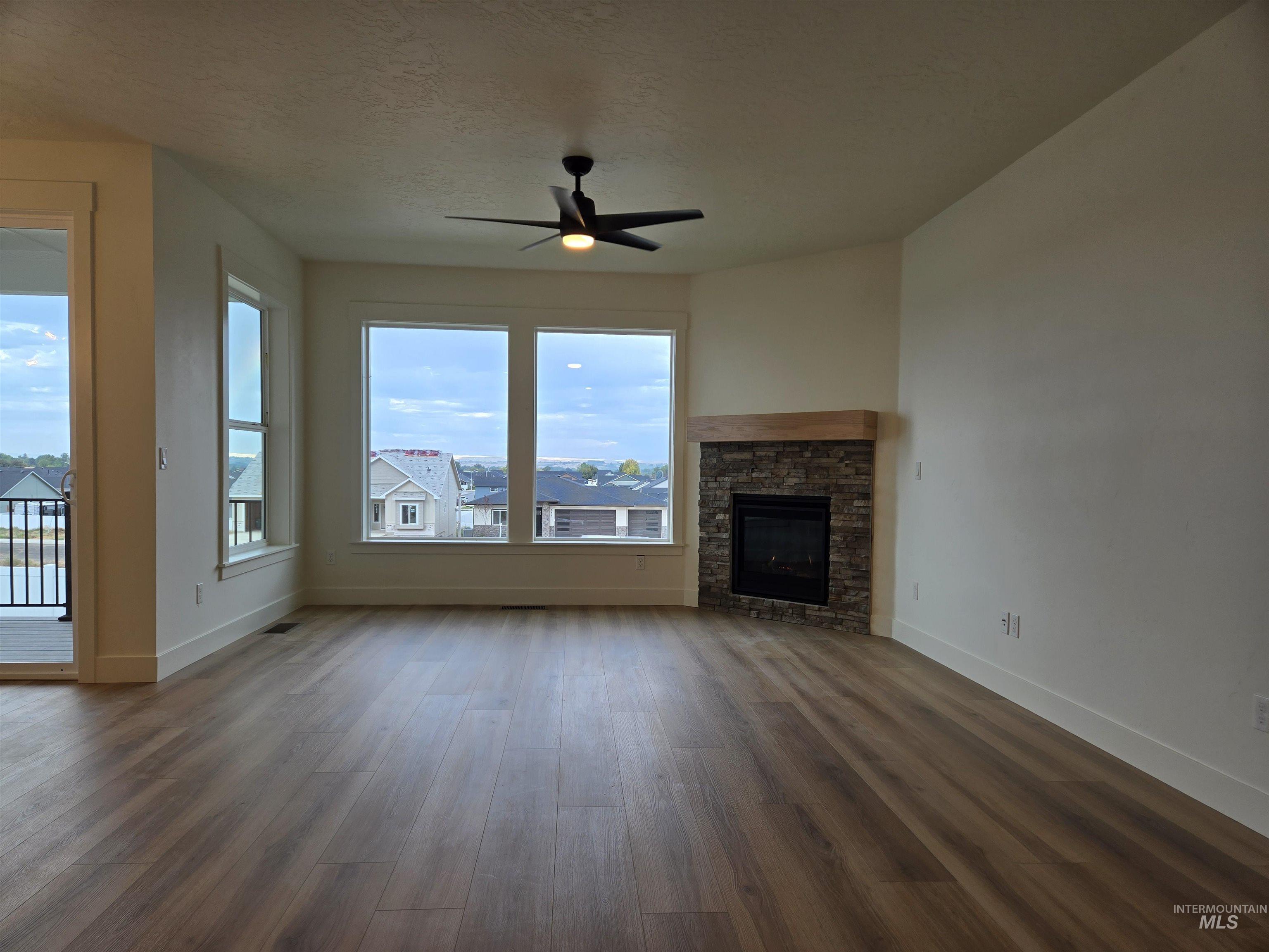 Unfurnished living room featuring a stone fireplace, a ceiling fan, plenty of natural light, dark wood finished floors, and a textured ceiling
