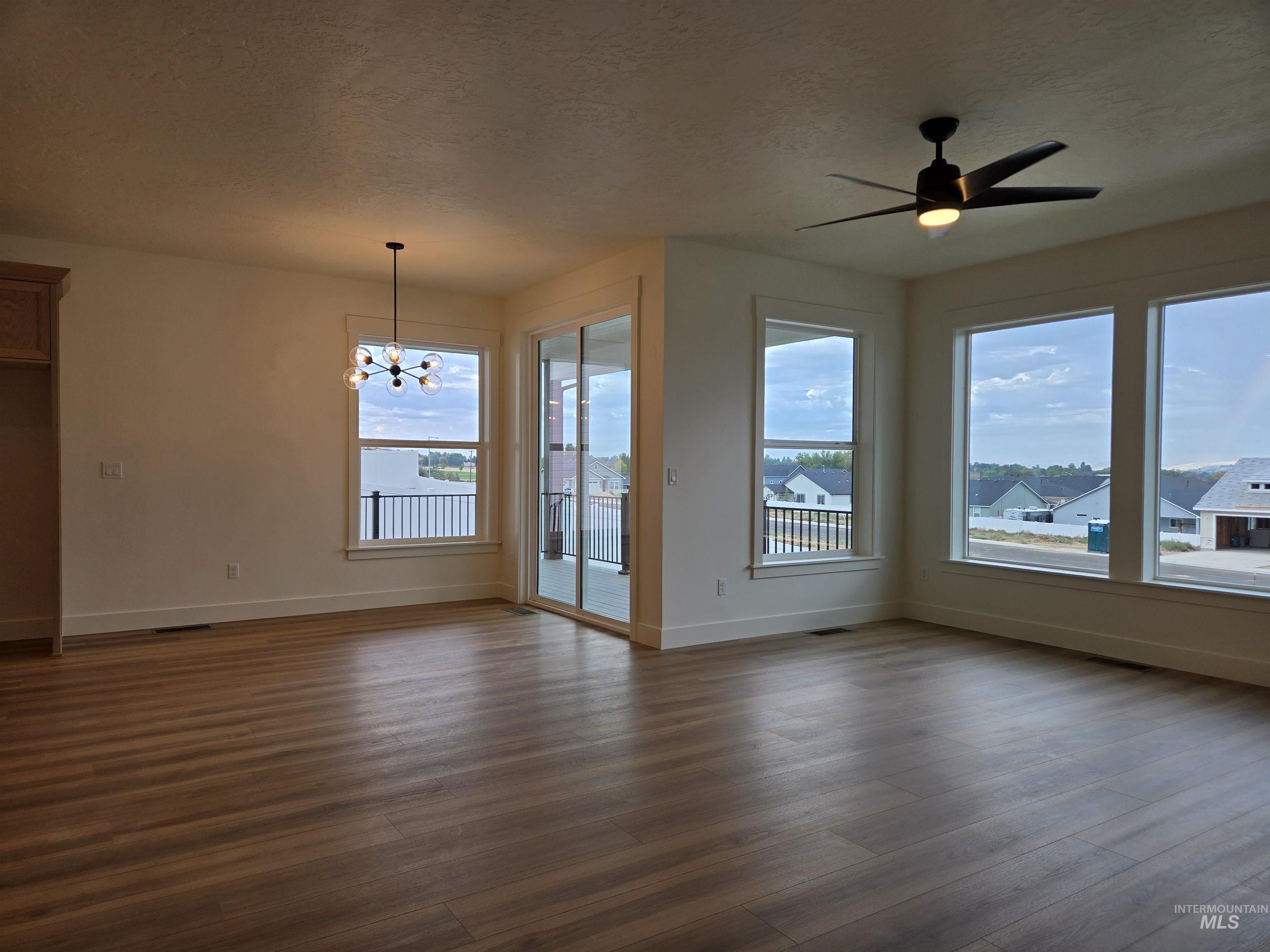 Unfurnished living room featuring a textured ceiling, ceiling fan, a chandelier, and dark wood-style floors