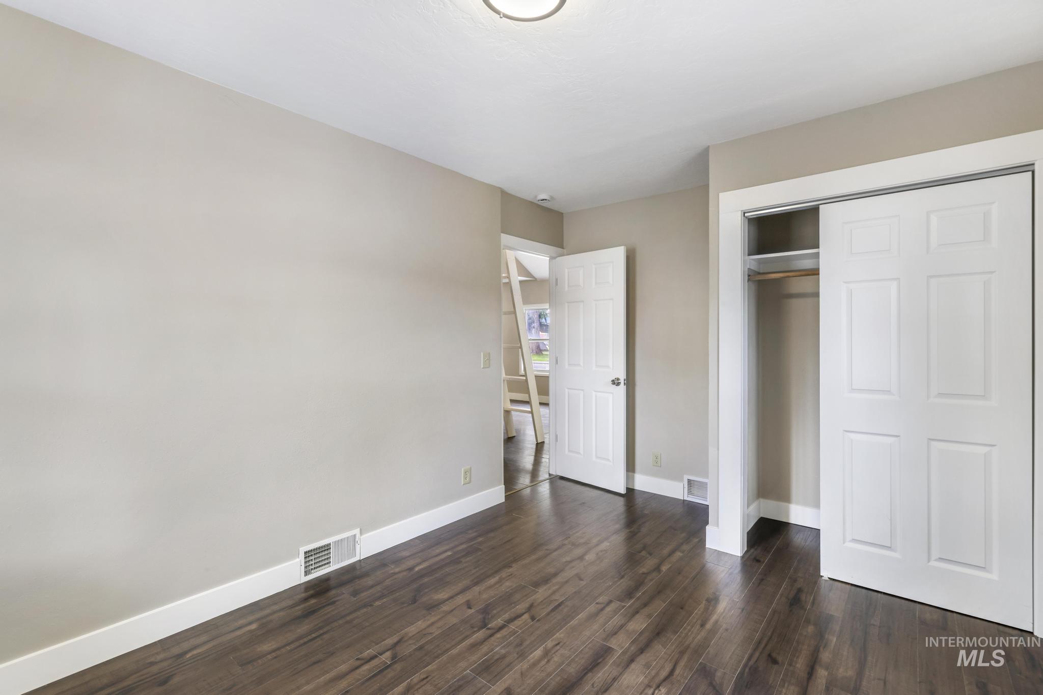 Unfurnished bedroom with dark wood-style floors and a closet