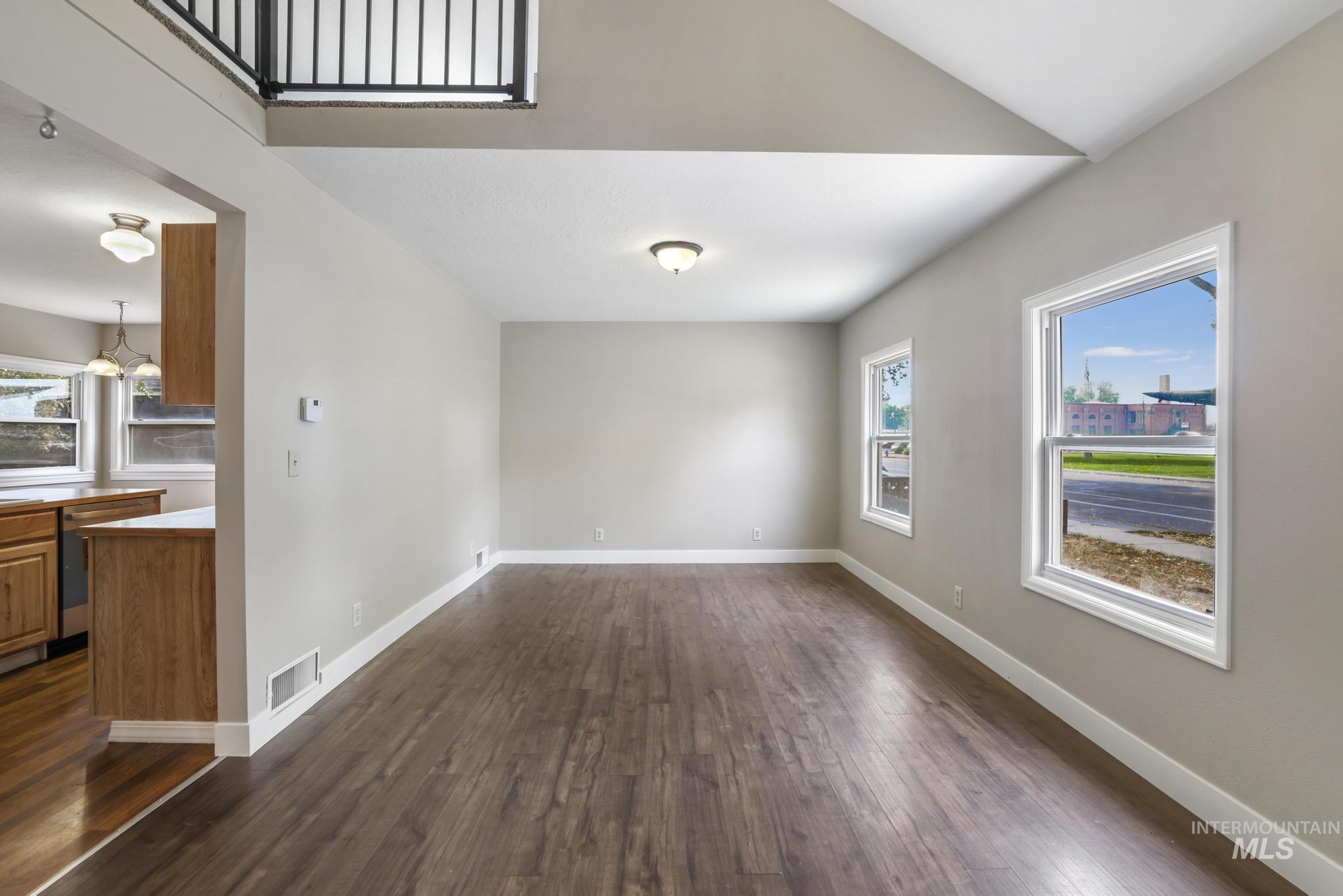 Unfurnished living room featuring dark wood-style flooring and baseboards