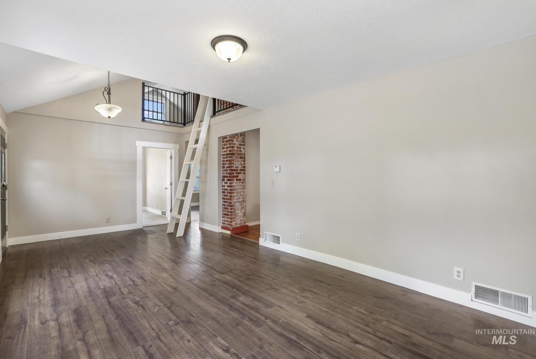 Empty room featuring dark wood-style floors and vaulted ceiling
