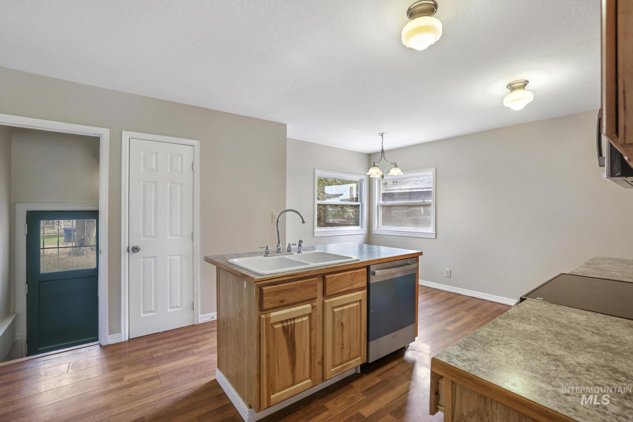 Kitchen featuring light countertops, dark wood finished floors, a kitchen island with sink, brown cabinets, and dishwasher