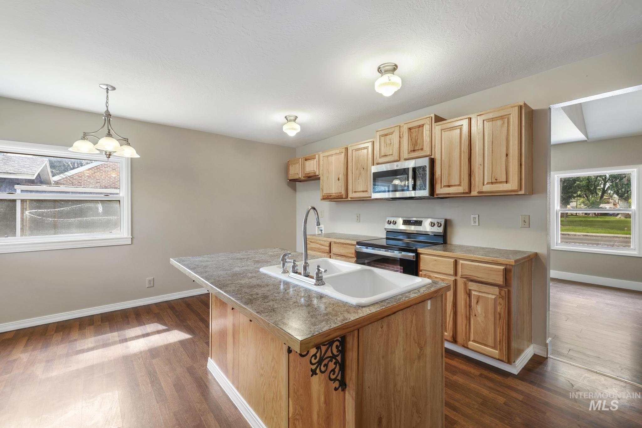 Kitchen with stainless steel appliances, dark wood finished floors, a kitchen island with sink, decorative light fixtures, and a chandelier