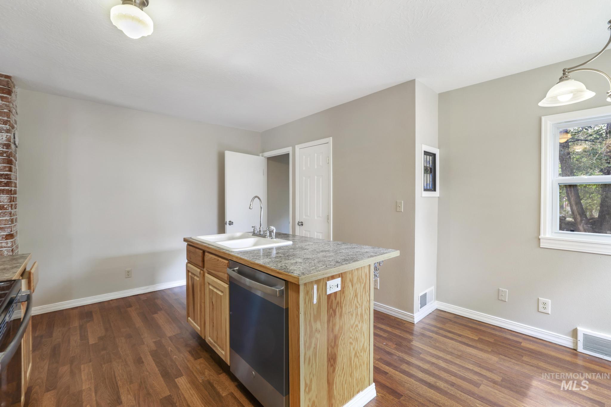 Kitchen featuring a center island with sink, light countertops, stainless steel appliances, and dark wood-type flooring