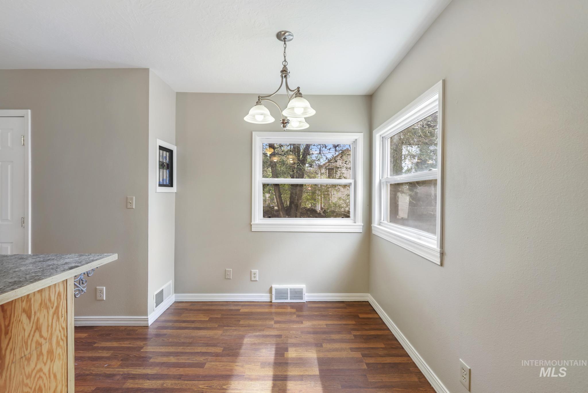 Unfurnished dining area featuring dark wood-style flooring and a chandelier