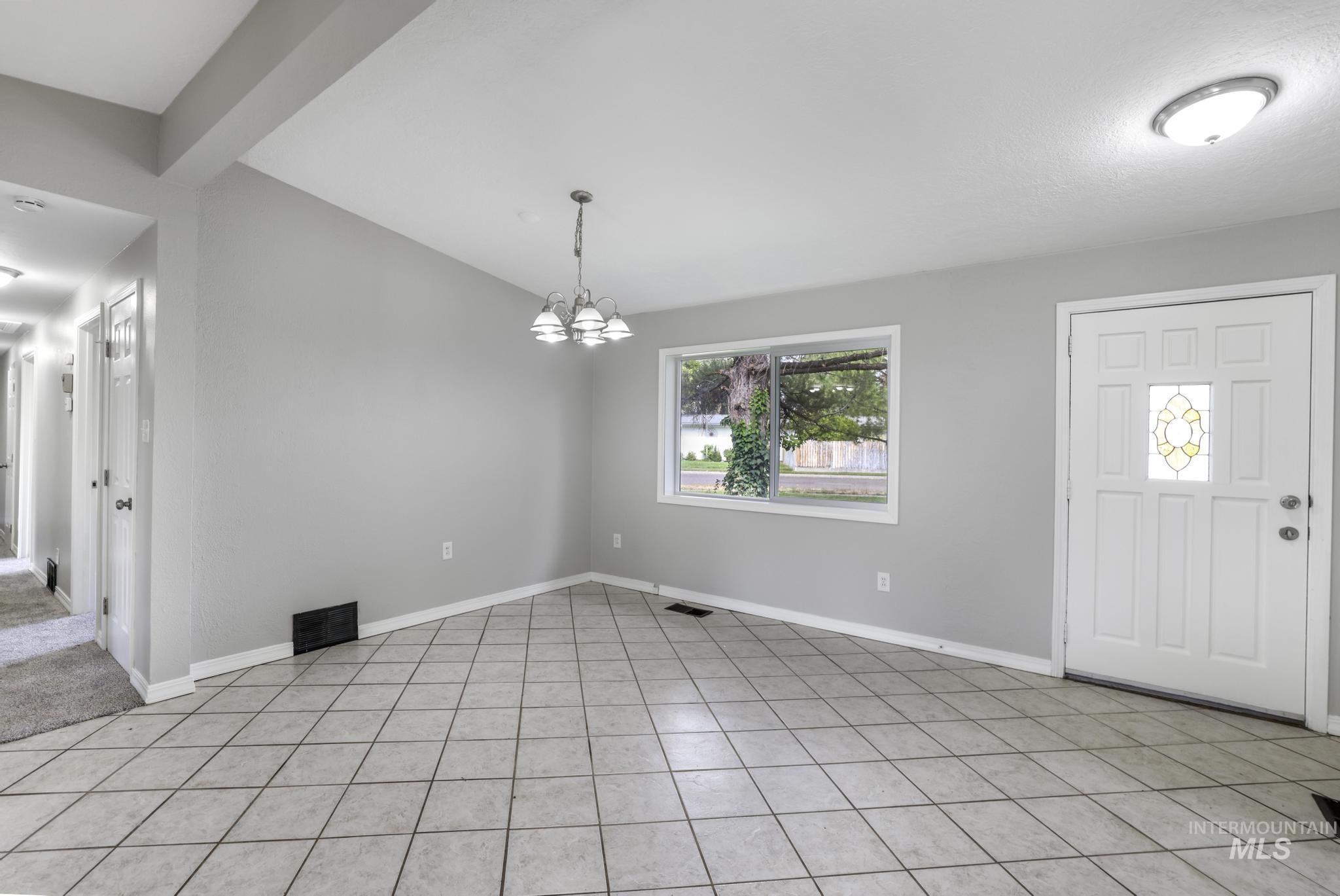 Foyer entrance with a chandelier, light tile patterned flooring, and beamed ceiling