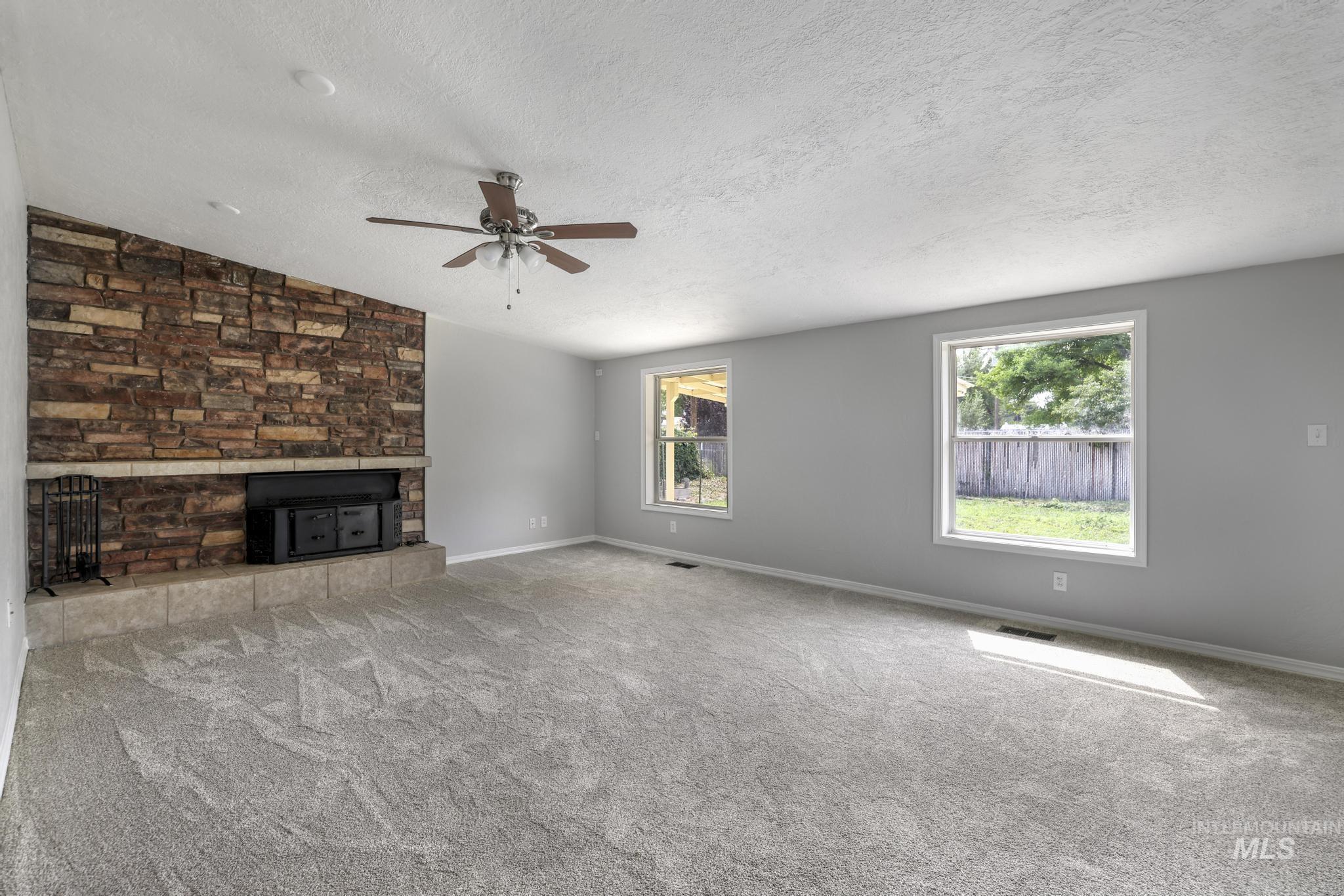 Unfurnished living room with a textured ceiling, carpet floors, and a ceiling fan