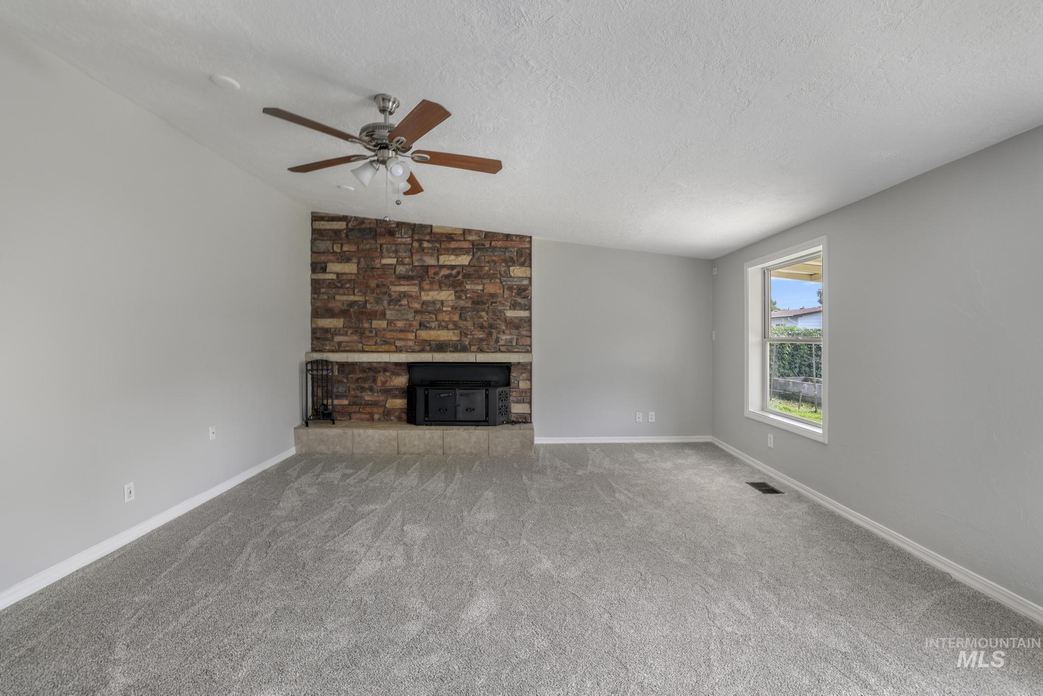 Unfurnished living room featuring lofted ceiling, ceiling fan, a textured ceiling, carpet, and a large fireplace